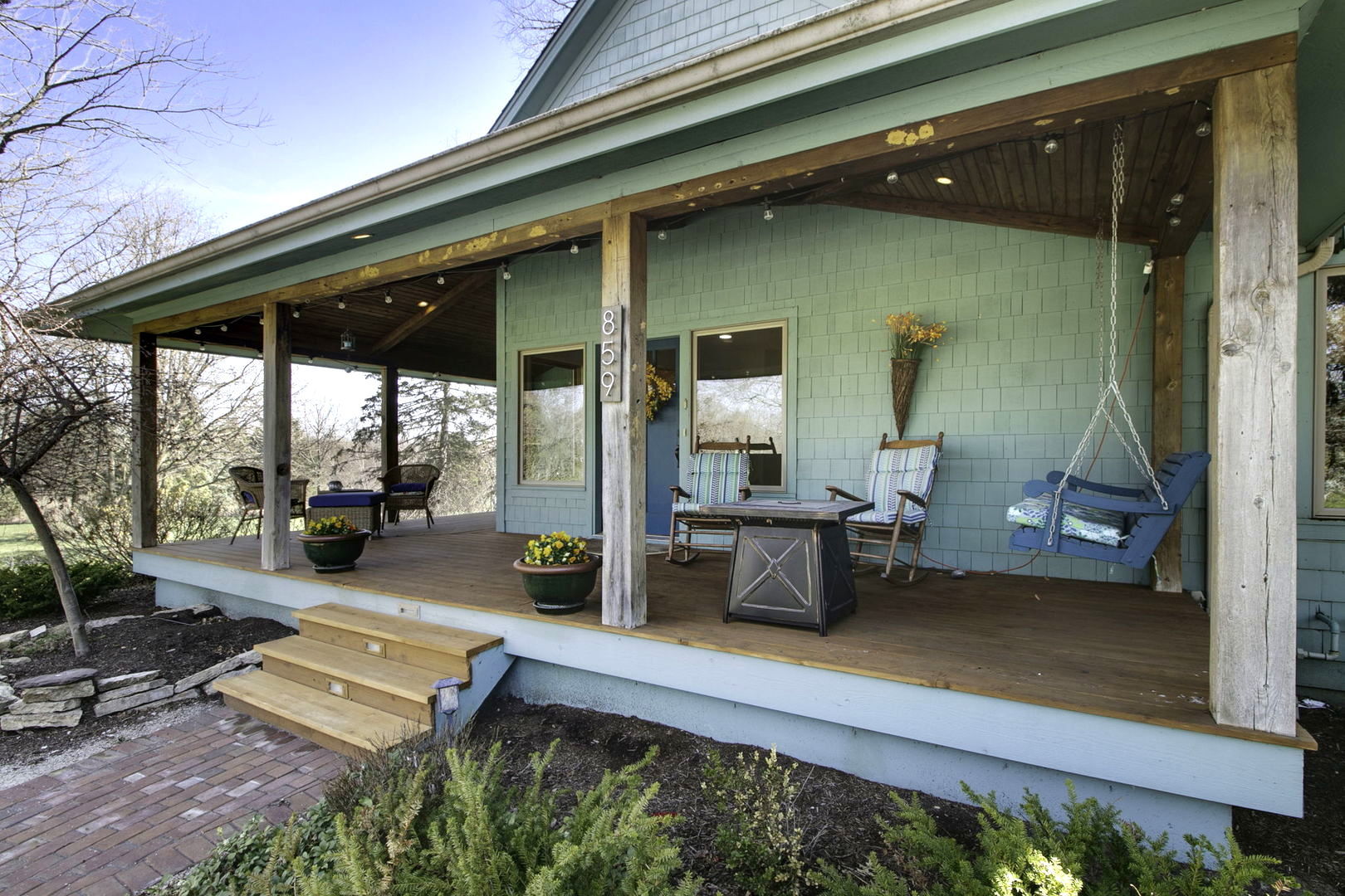 Covered front porch with green shingle siding, timber beams, wooden steps, and a hanging swing.