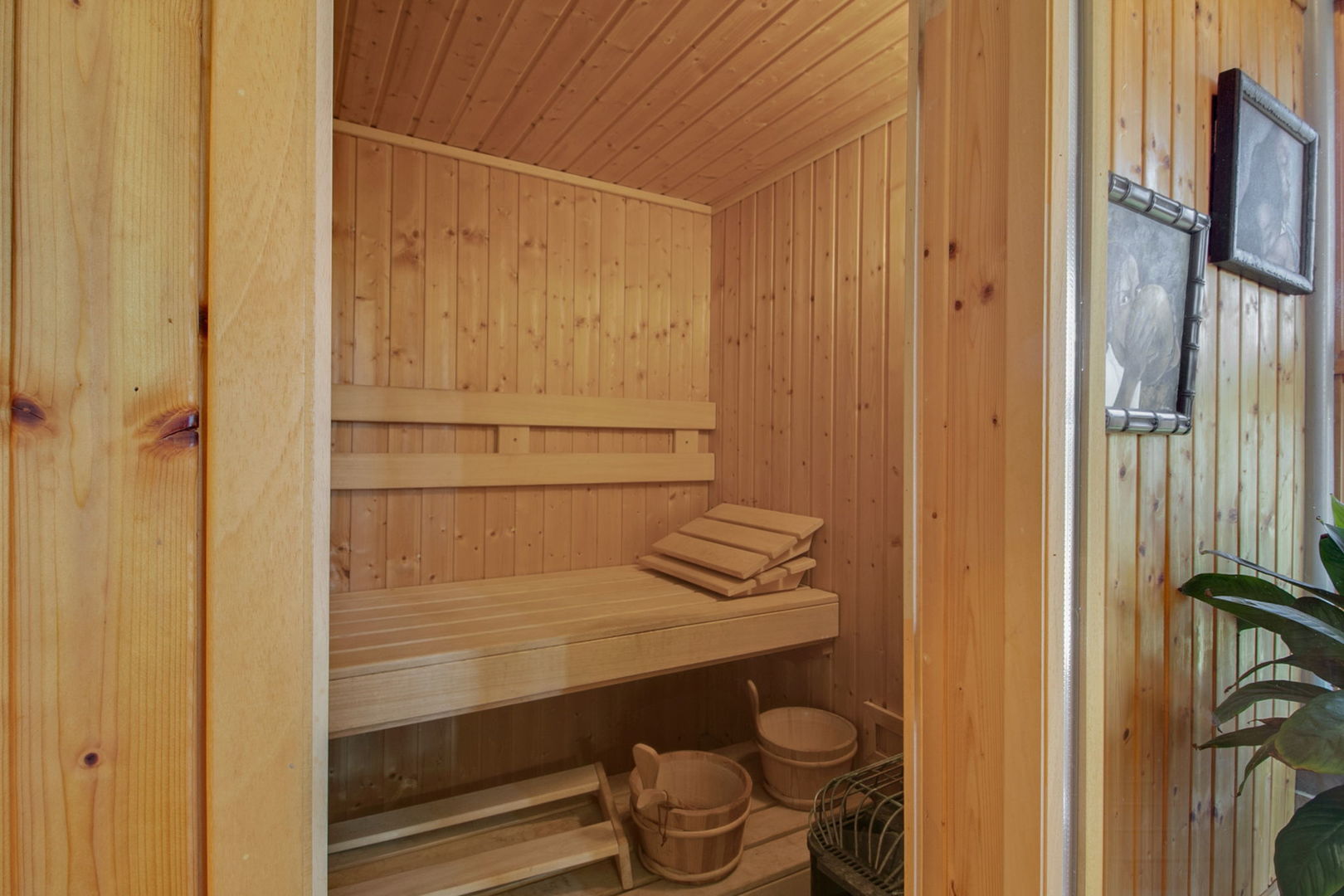 Wood-paneled sauna with tiered benches, wooden buckets, and a heater.