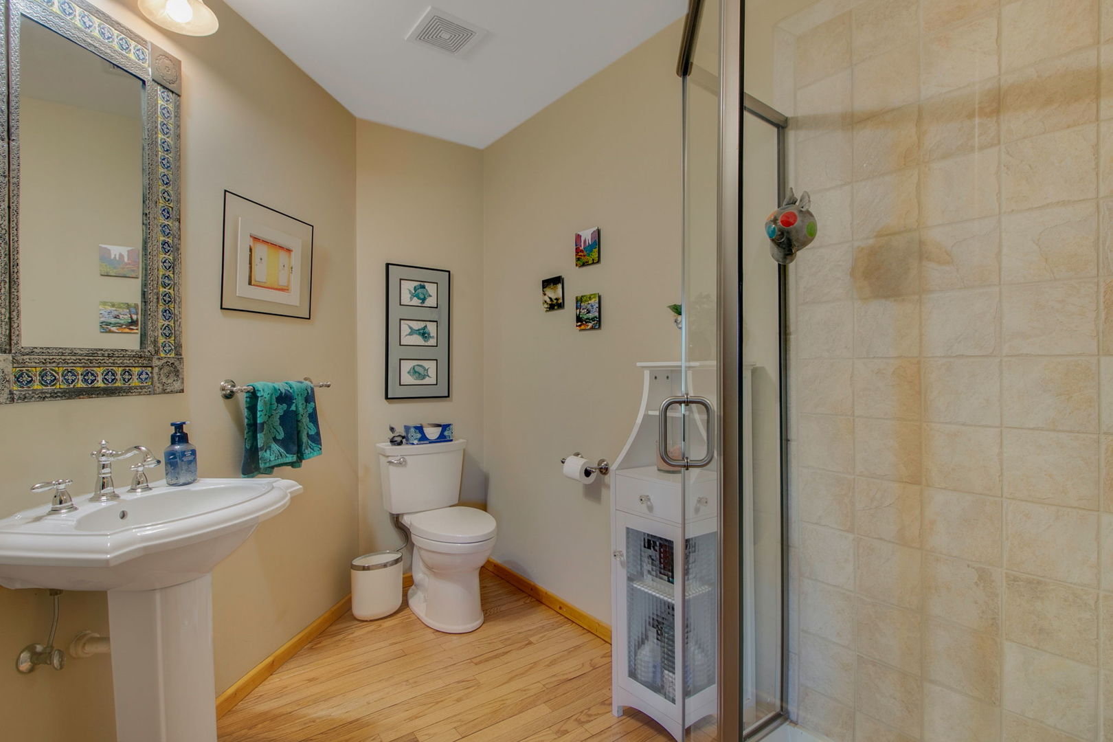 Bathroom with a pedestal sink, wood flooring, and a glass shower with beige stone tile.