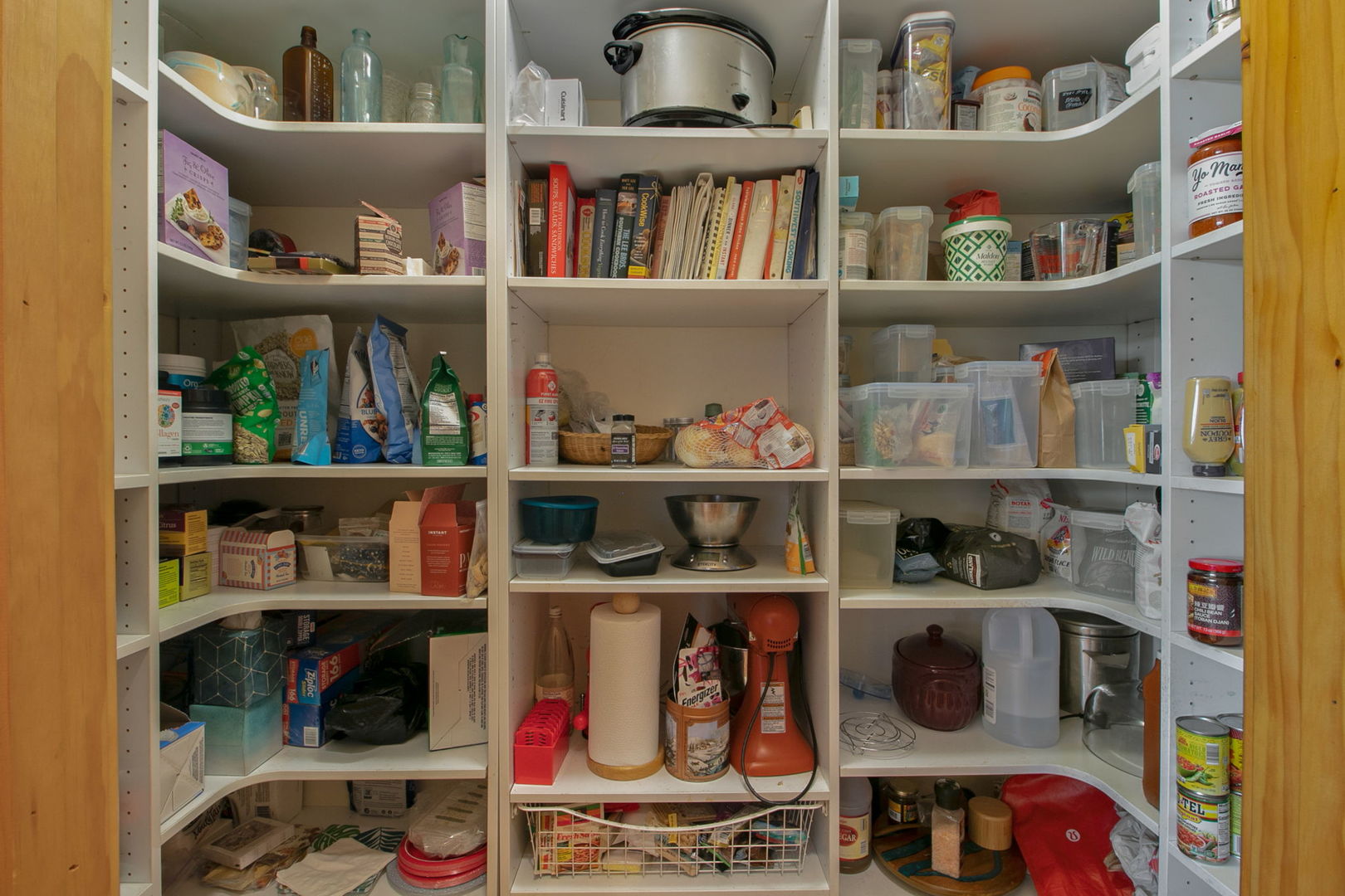 Walk-in pantry lined with stocked white shelves and a wire basket.
