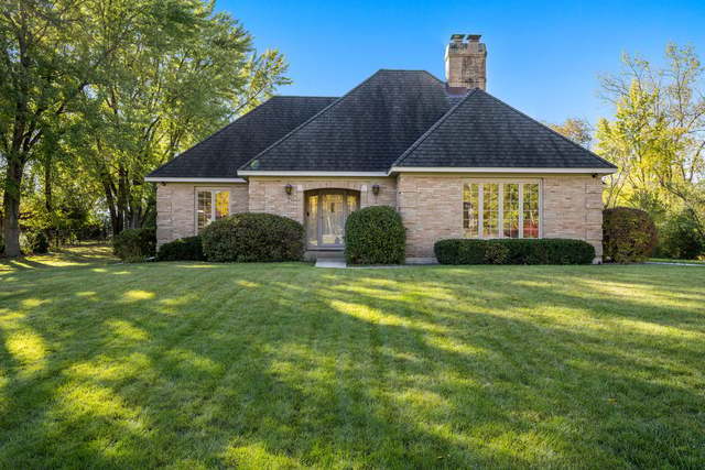 Brick house with a dark hipped roof and chimney, framed by mature trees and a broad lawn.