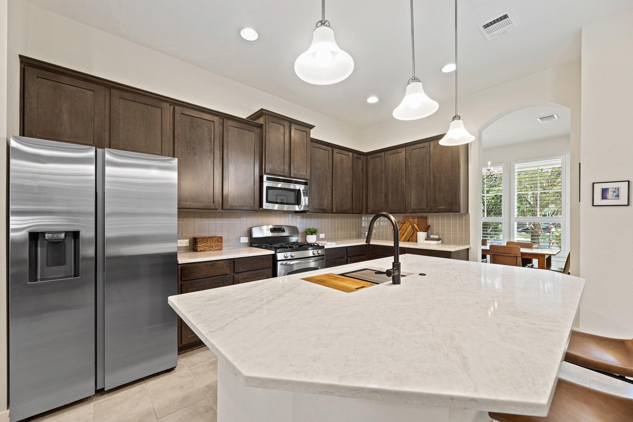 Kitchen with dark wood cabinets, stainless appliances, and a large white island with an integrated sink.