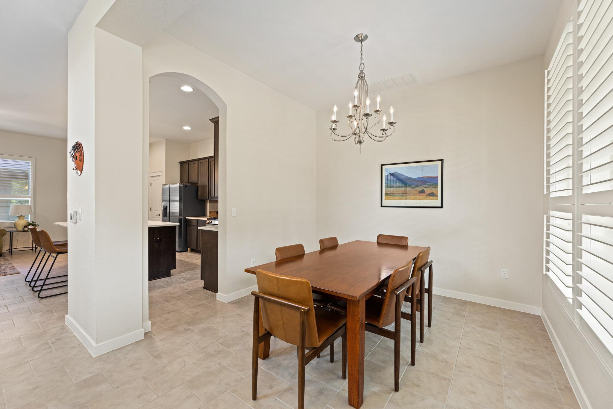 Dining room with a wooden table, leather chairs, chandelier, and plantation shutters.