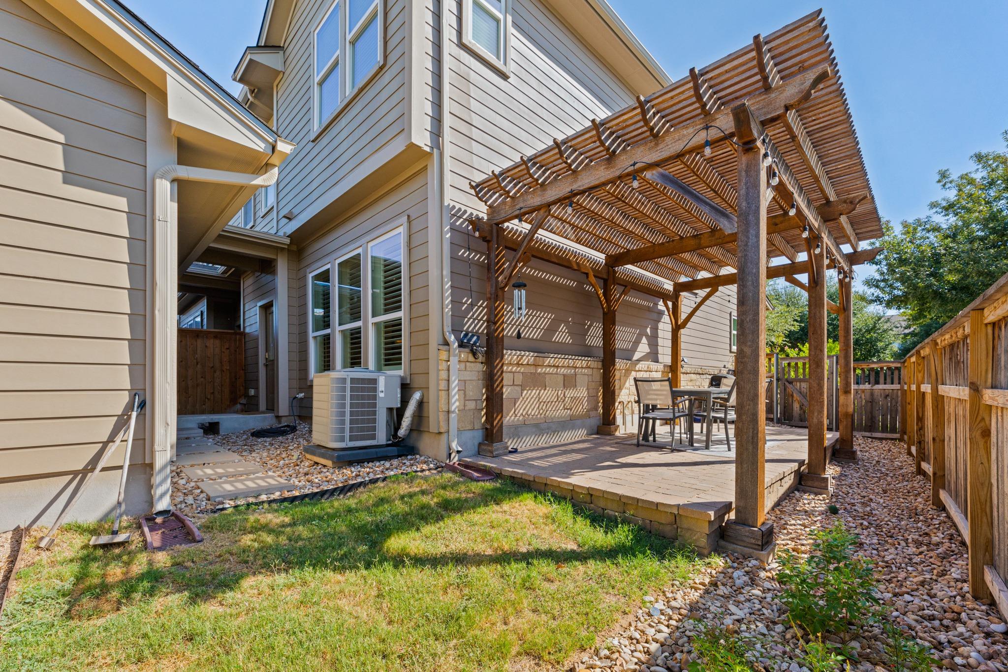 Fenced backyard patio with a wooden pergola, raised deck, and outdoor dining set.