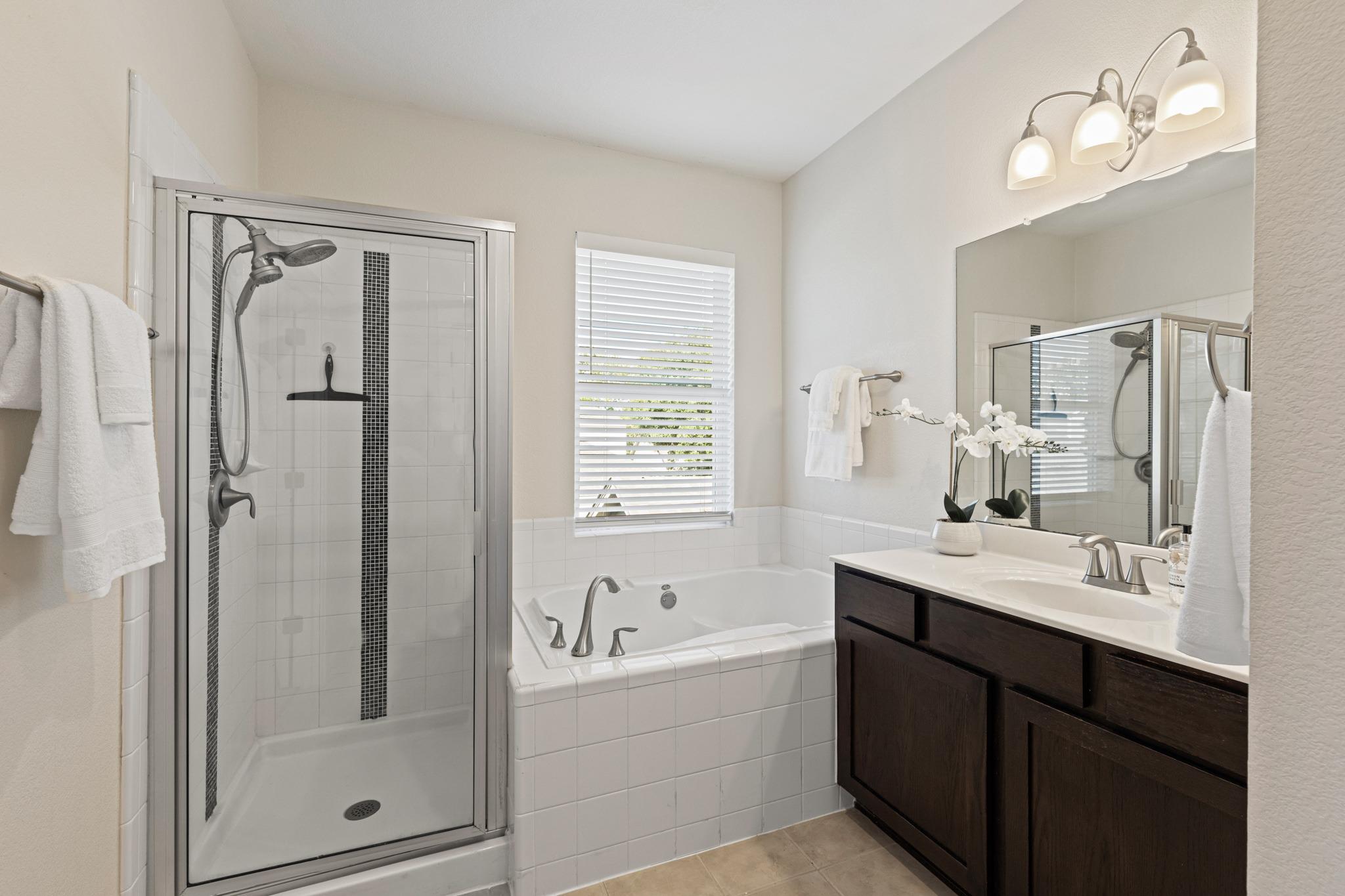 Bathroom with glass shower, soaking tub, and dark wood double vanity.