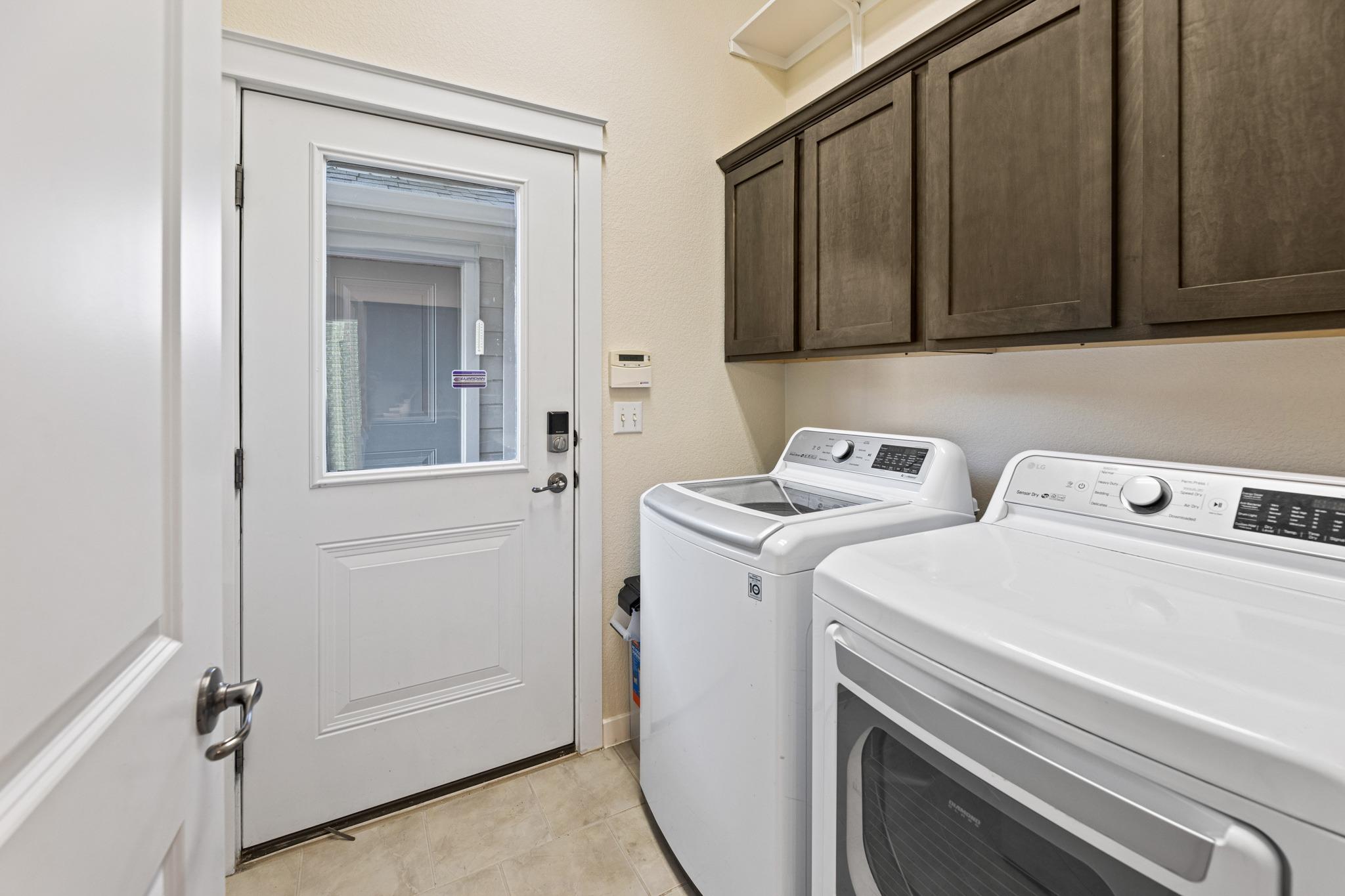 Laundry room with a top-loading washer, front-loading dryer, dark cabinets, and a windowed exterior door.