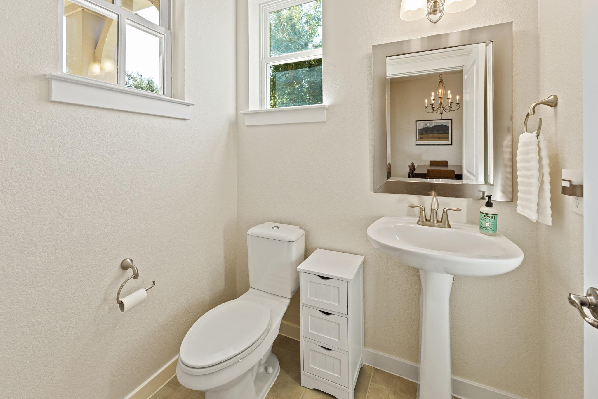Bathroom with a pedestal sink, toilet, high windows, and a mirror reflecting a dining room.