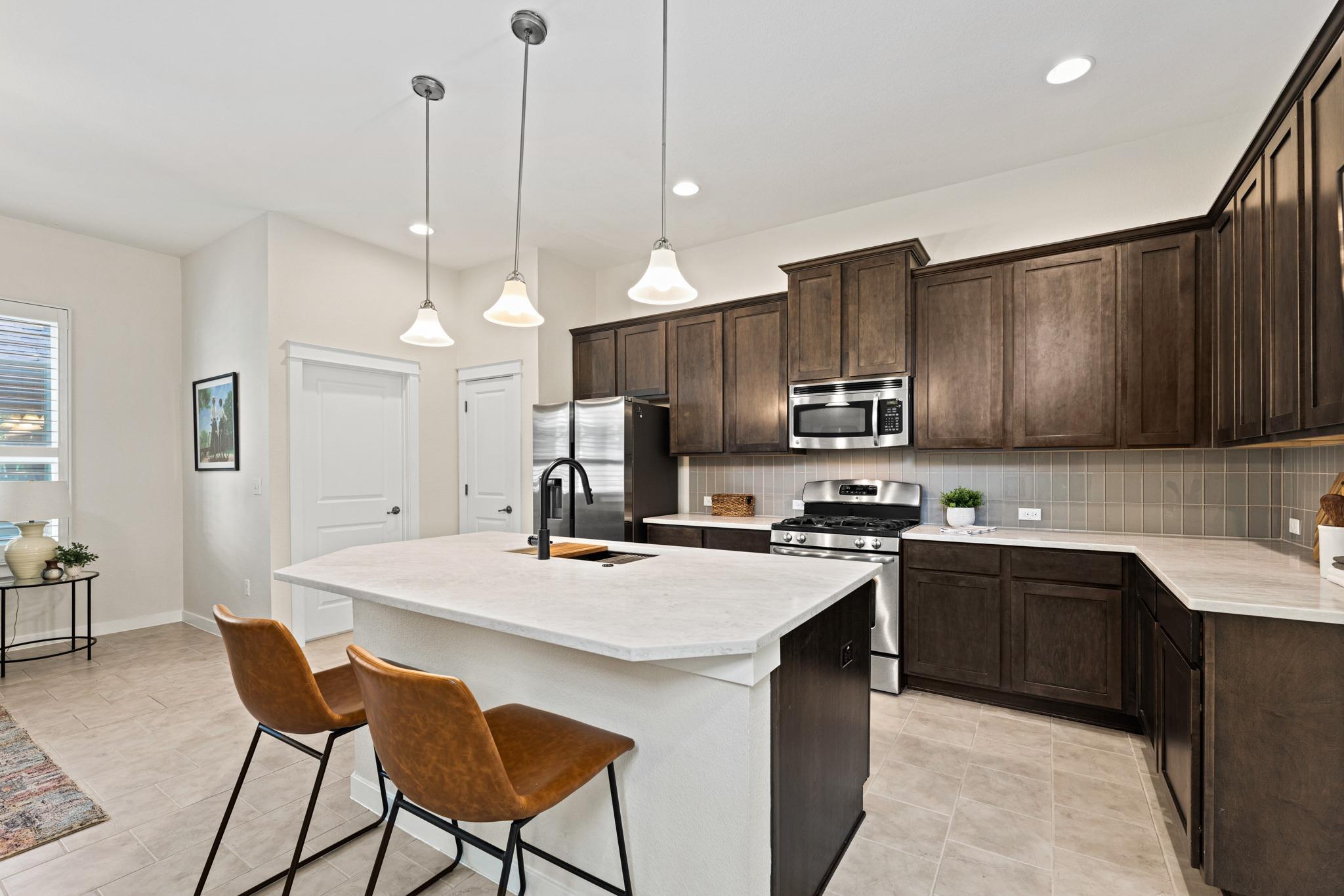 Kitchen with dark wood cabinets, stainless appliances, and a large white island with two brown chairs.