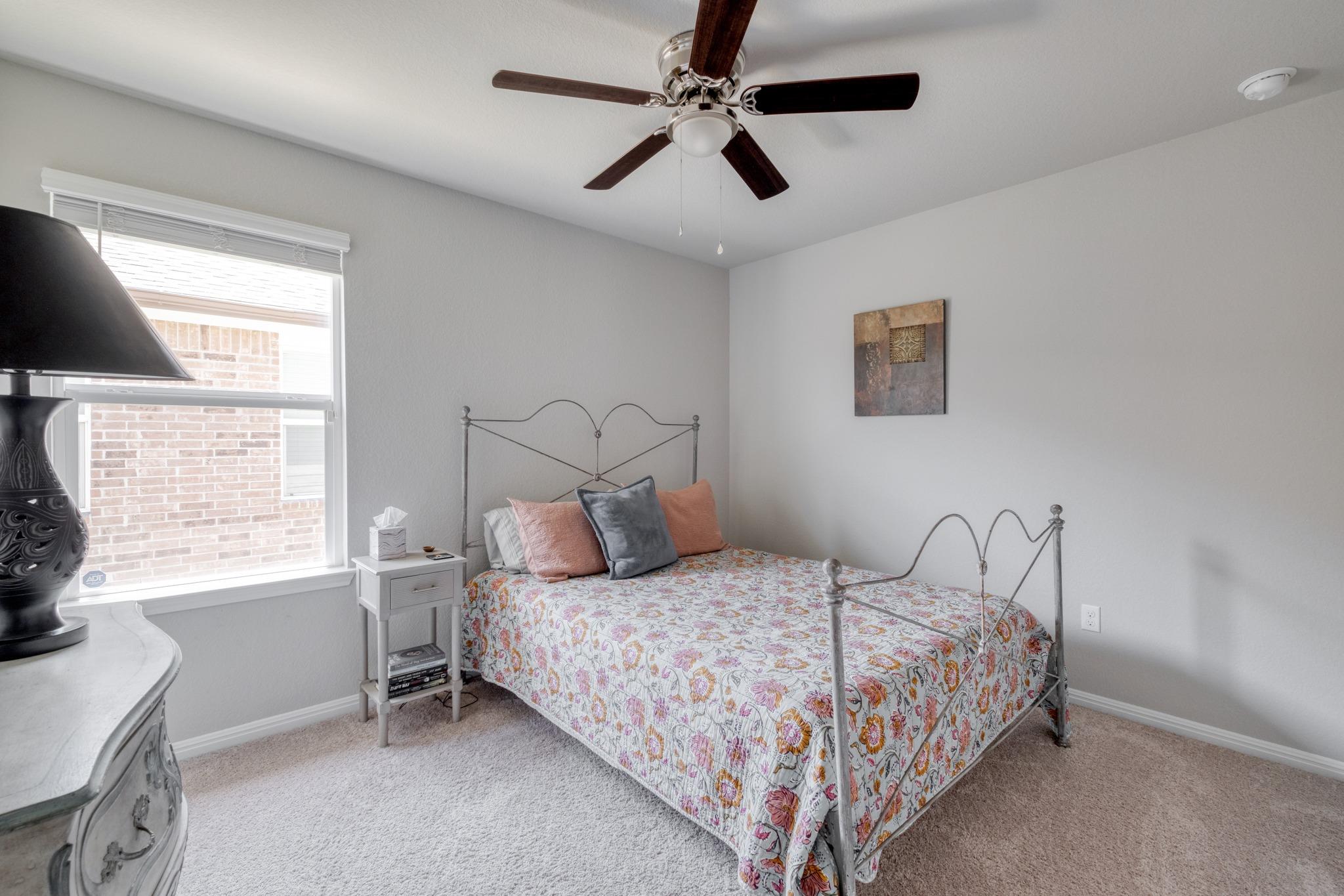 Bedroom with a metal bed frame, floral quilt, and window overlooking a brick wall.