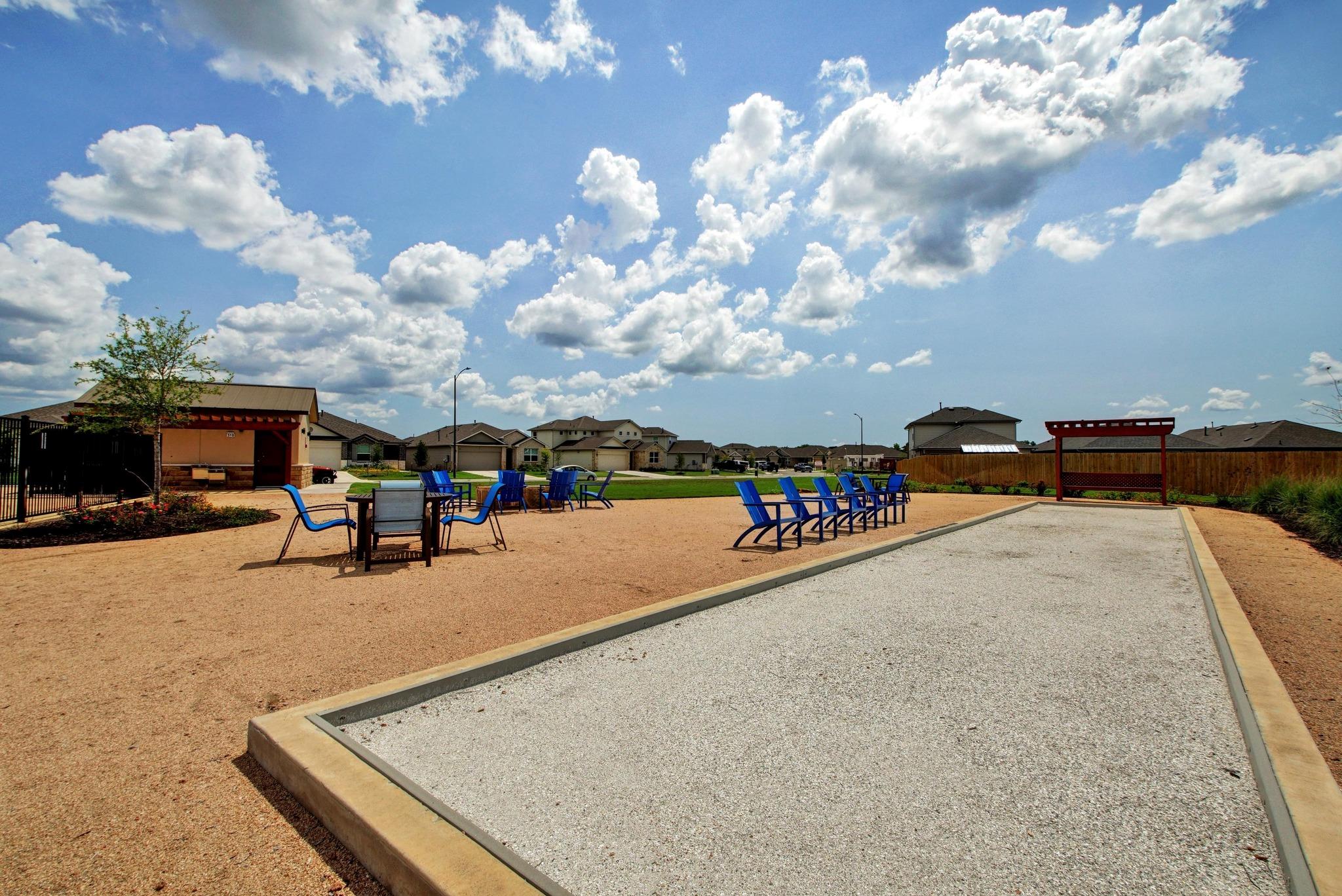 Community bocce ball court with blue seating, picnic tables, and a small pavilion.