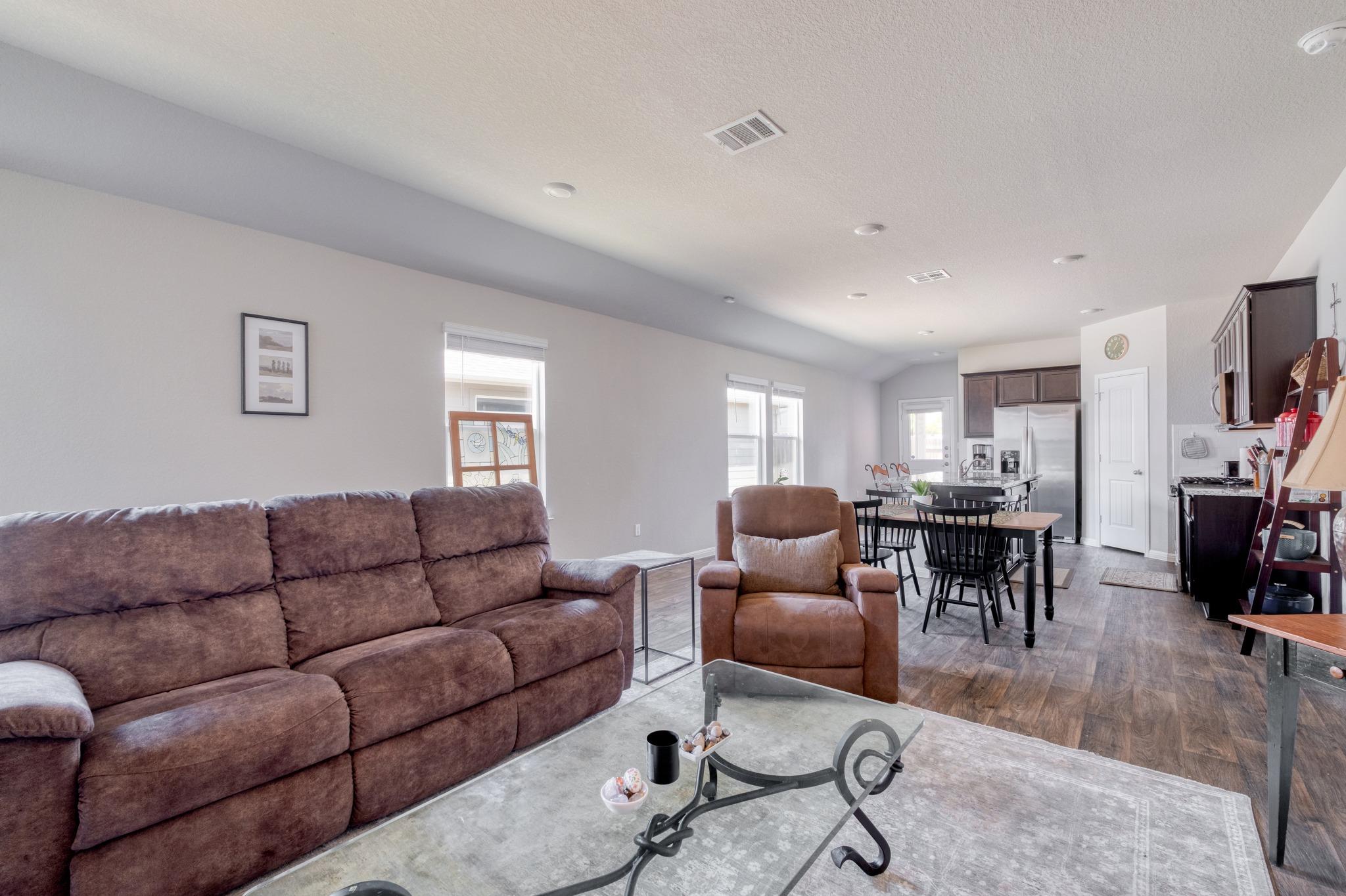 Open-plan living room with a brown sectional and recliner beside the dining area and kitchen.