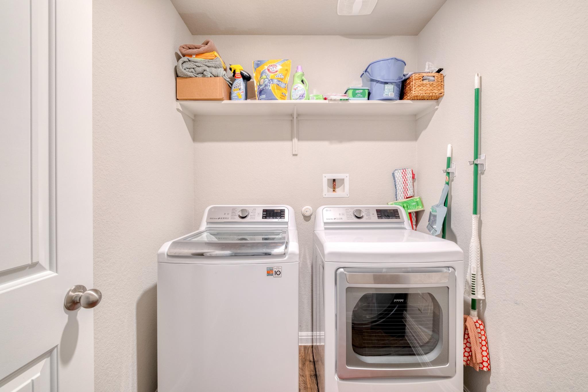 Laundry room with a washer and dryer, a supply shelf, and cleaning tools.