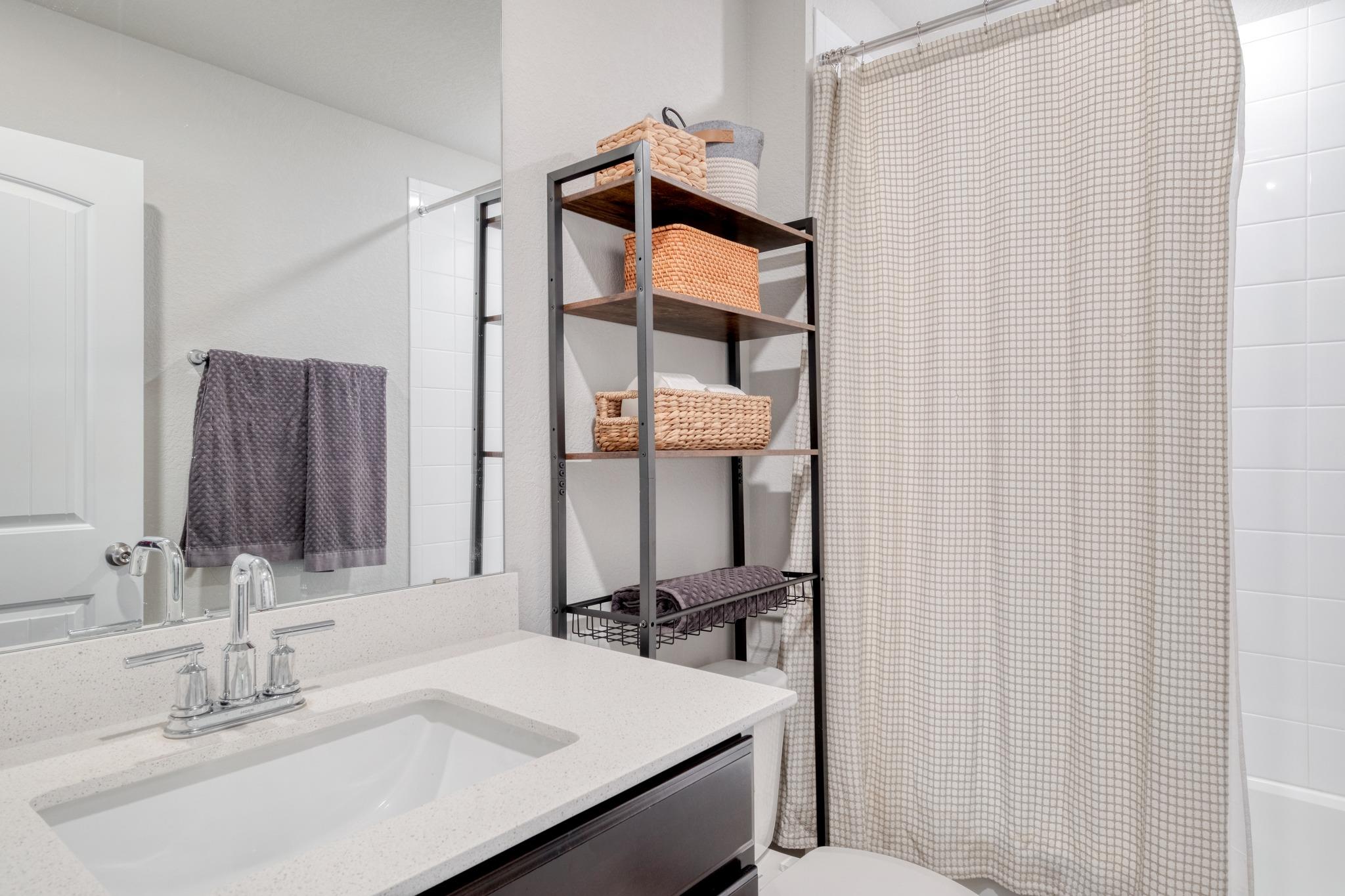 Bathroom with a white sink, large mirror, and patterned shower curtain beside open towel shelving.