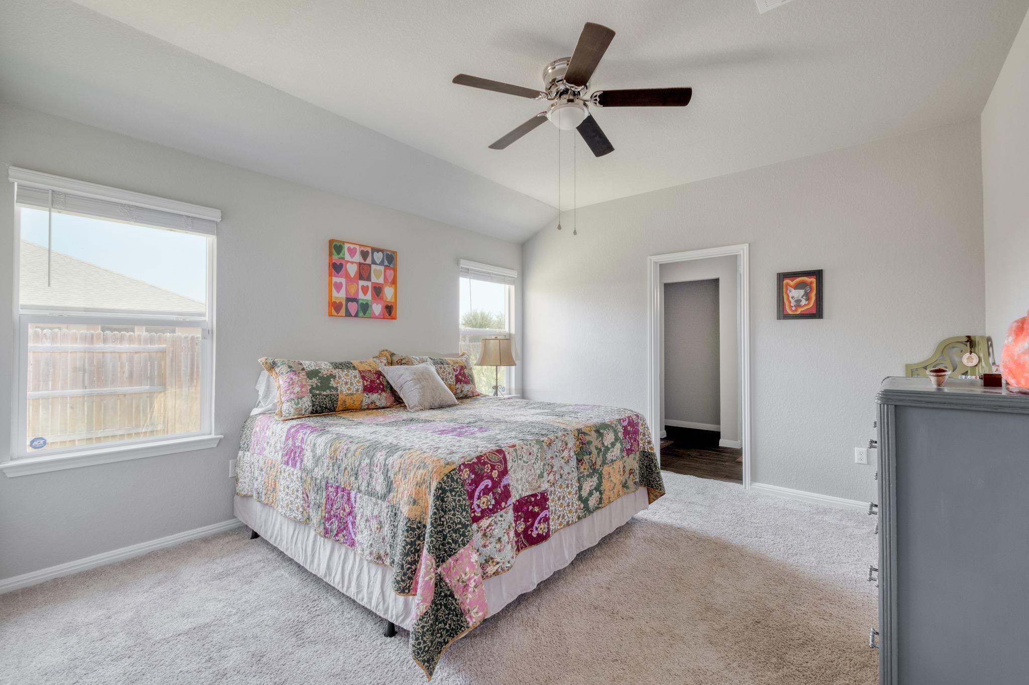 Bedroom with a colorful patchwork quilt, vaulted ceiling, and ceiling fan.
