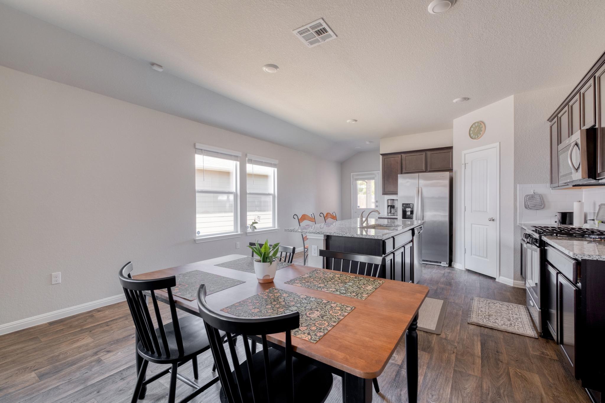 Open kitchen and dining area with a wooden table, dark cabinets, and stainless steel appliances.