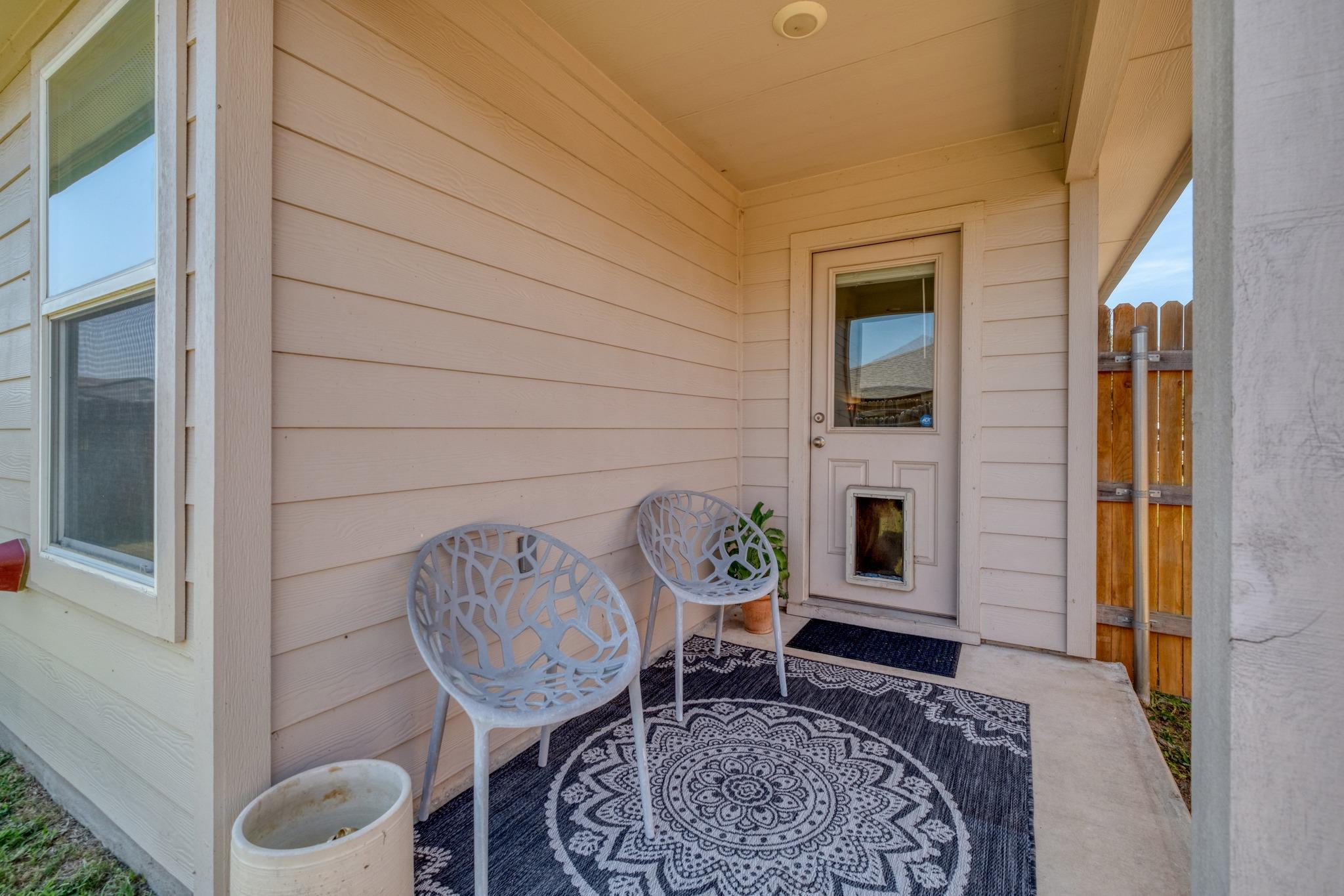 Covered porch with two white chairs, a patterned rug, and an entry door with a pet door.