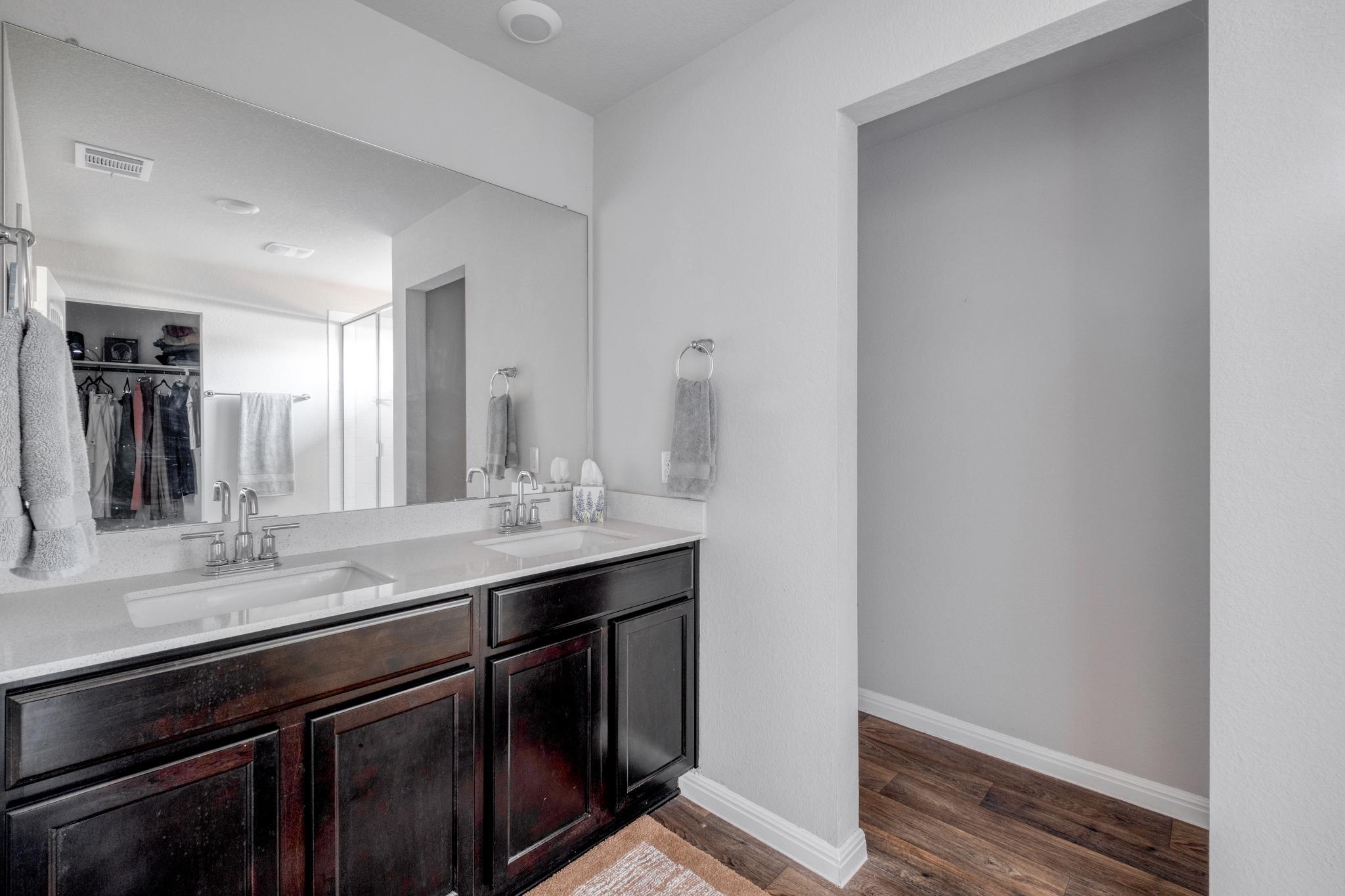 Bathroom with a double-sink vanity, dark wood cabinets, and a large mirror reflecting an open closet.