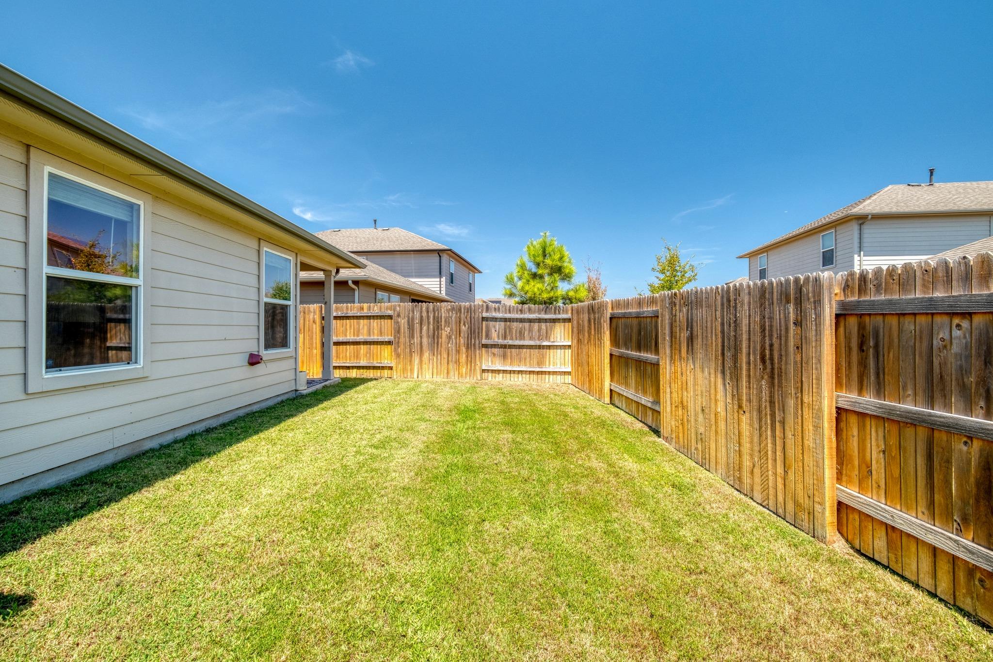 Fenced backyard with a broad grassy lawn beside a light-sided house.