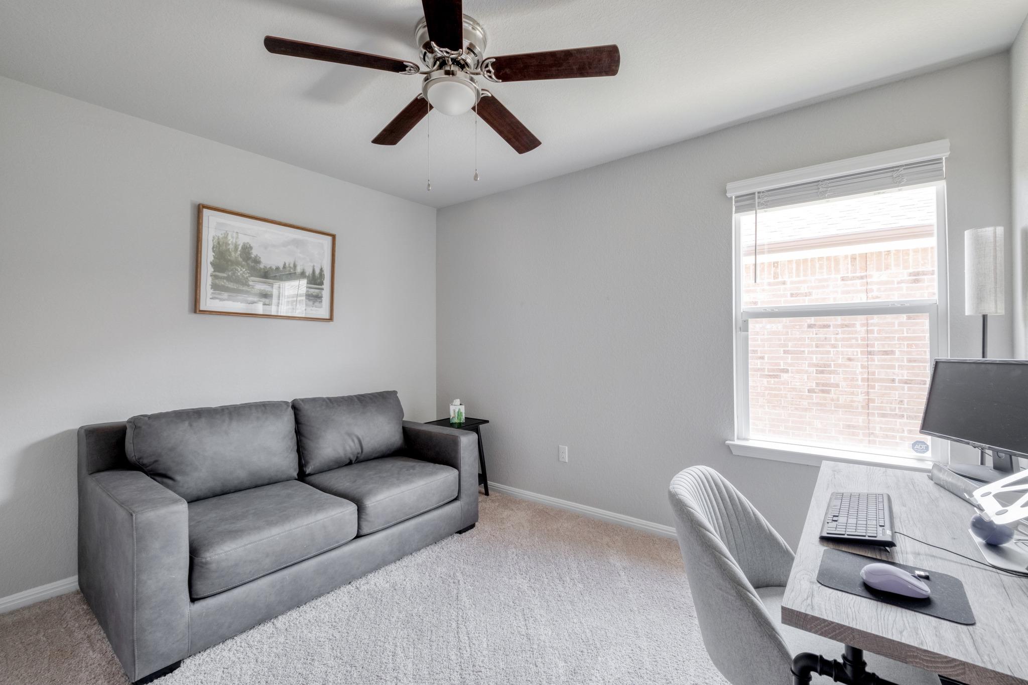 Home office with a gray sofa, computer desk, and ceiling fan.