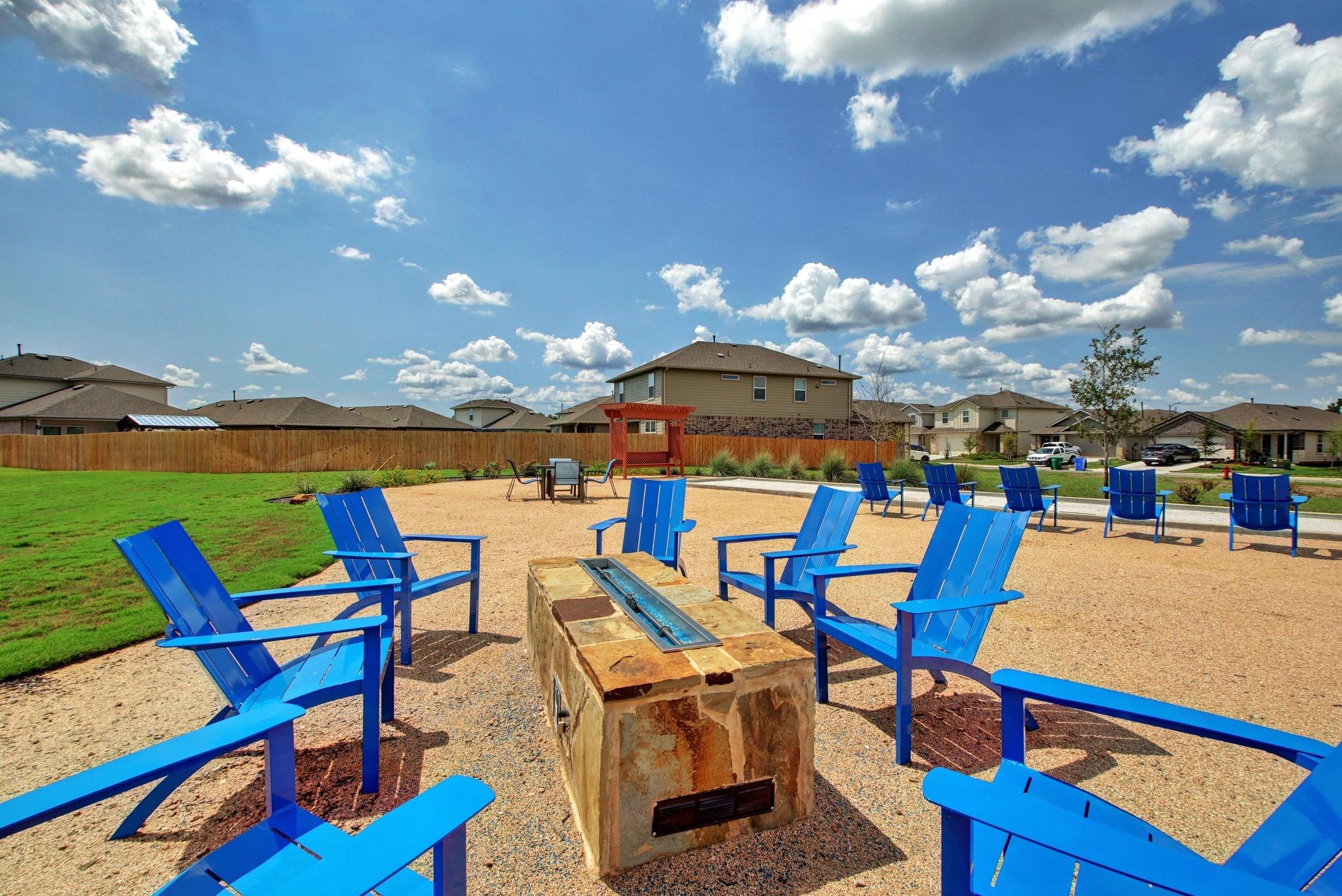 Community fire pit surrounded by blue Adirondack chairs on a gravel patio.