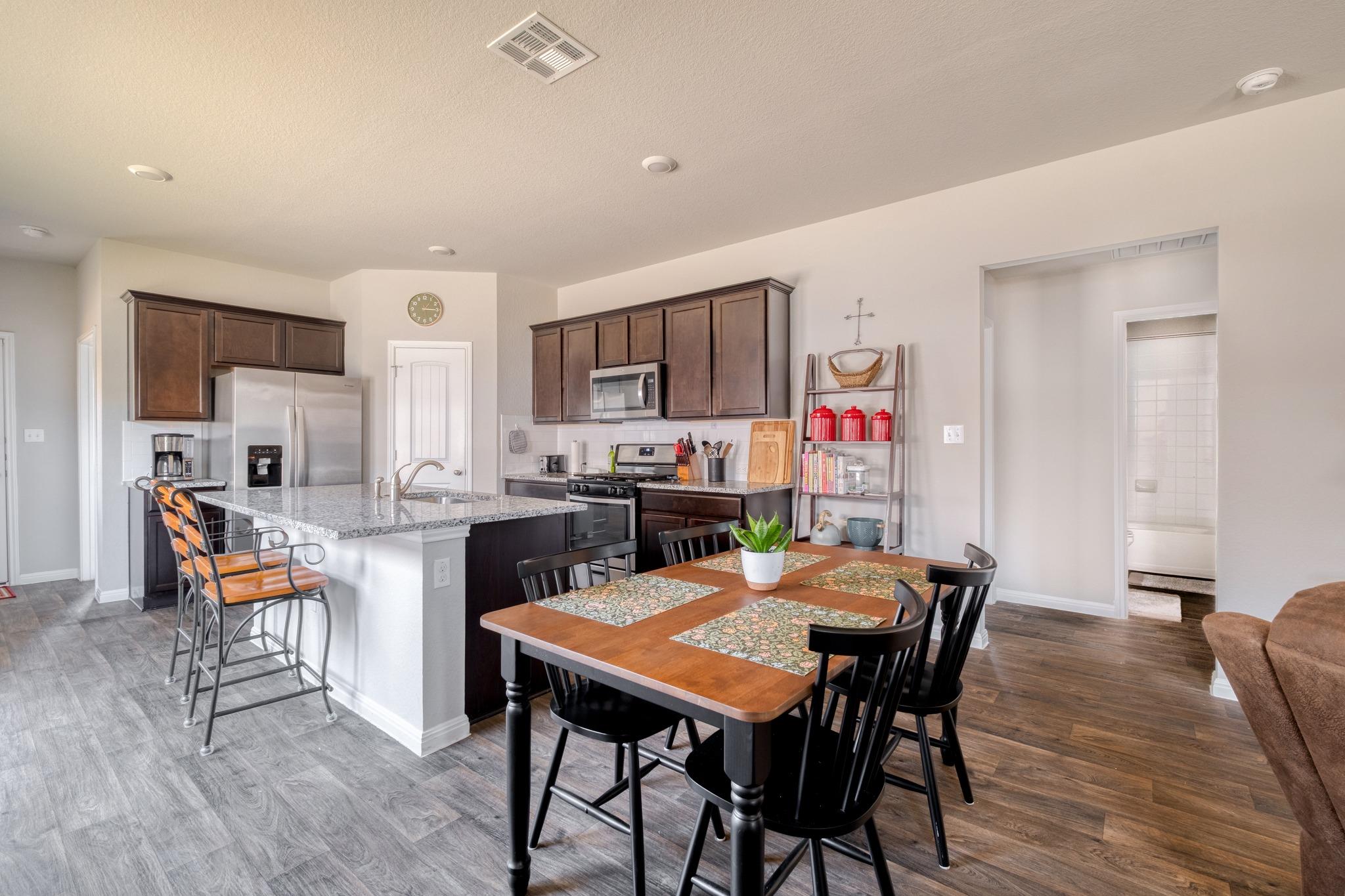 Open kitchen and dining area with a granite island, dark cabinets, and a wooden dining table.