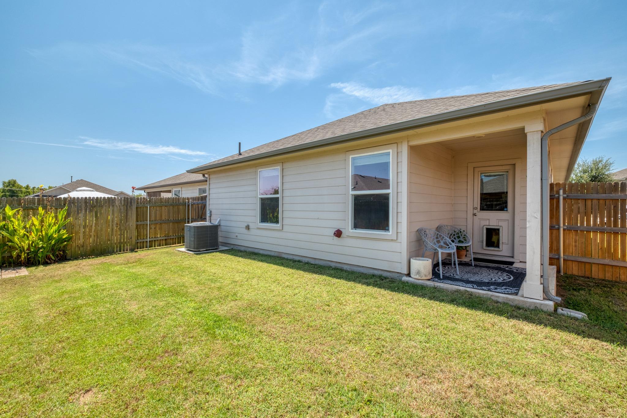 Home’s rear exterior with a covered patio, fenced grassy backyard, and outdoor air-conditioning unit.