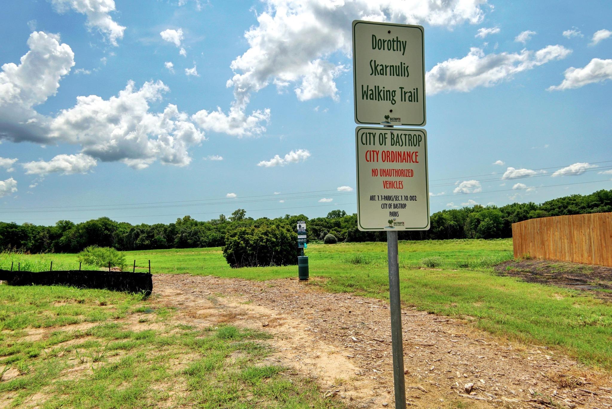 Dorothy Skarnulis Walking Trail entrance, marked by a tall sign beside an open grassy path.