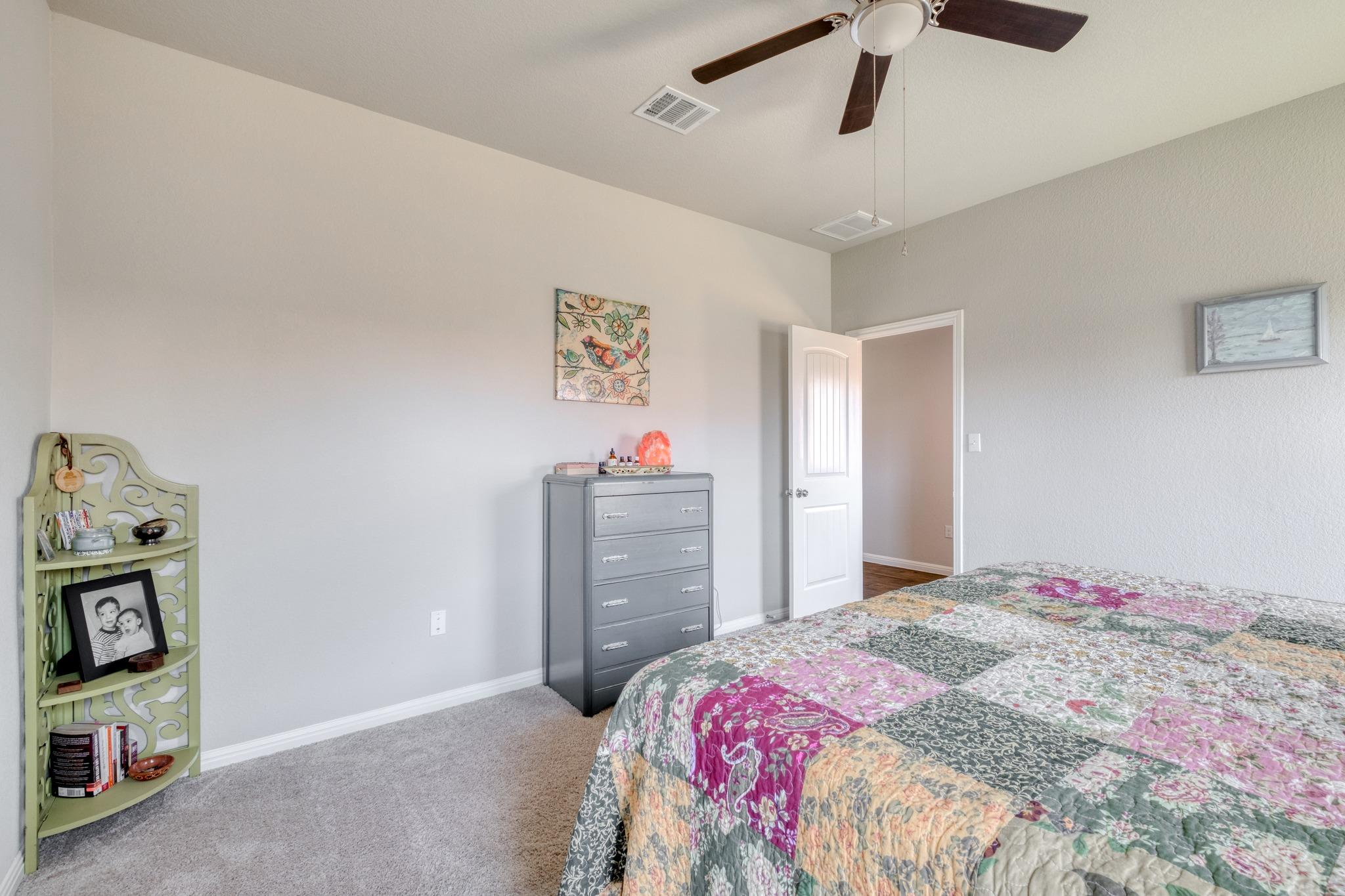 Bedroom with a colorful floral quilt, gray dresser, and pale green corner shelf.