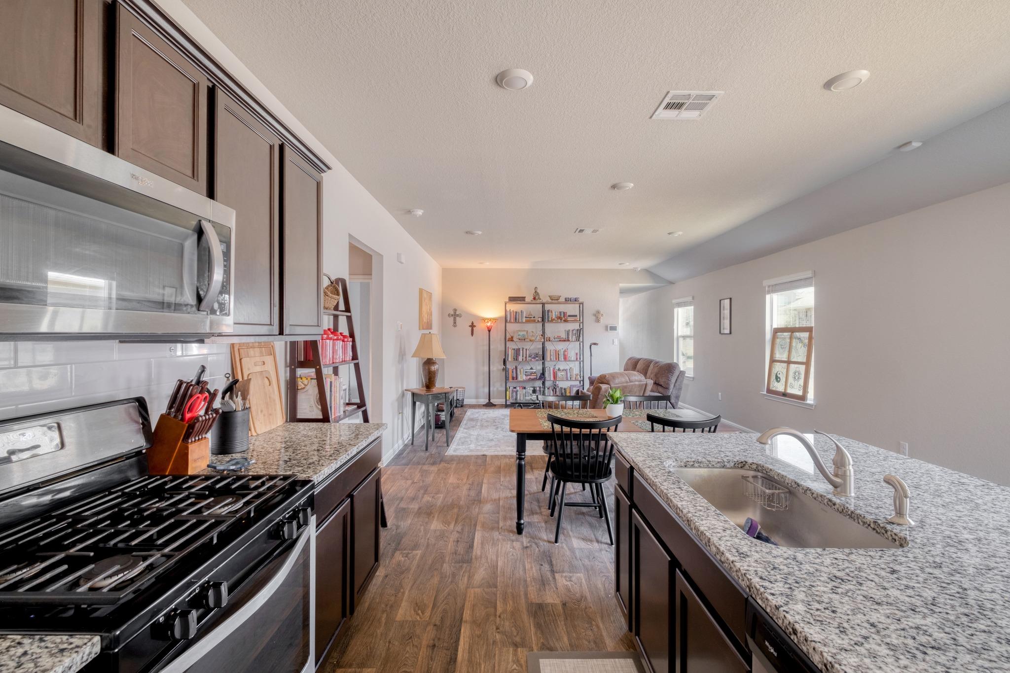 Kitchen opening into a living room, with granite countertops and dark wood cabinets.