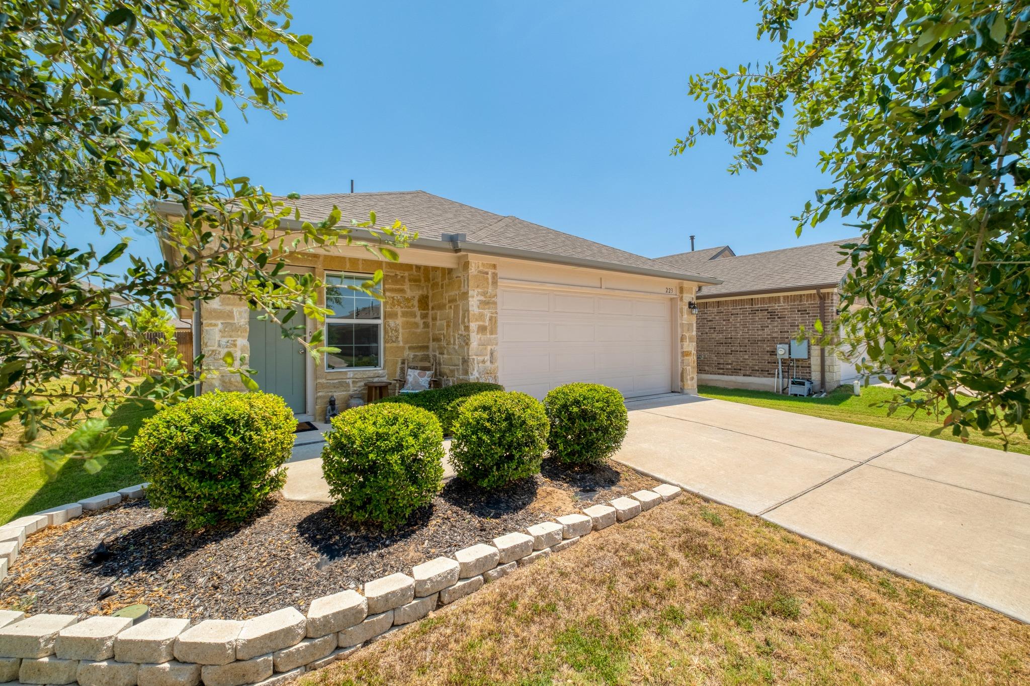 Single-story stone-front home with a two-car garage, wide driveway, and trimmed shrubs.