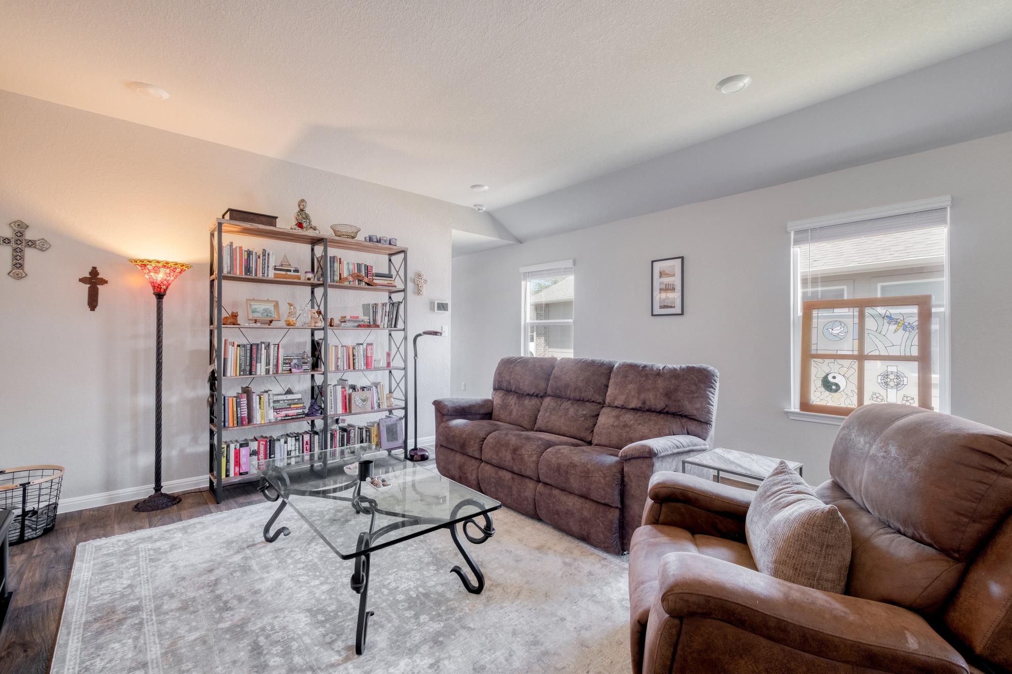 Living room with brown reclining sofas, a glass coffee table, and a book-filled bookcase.