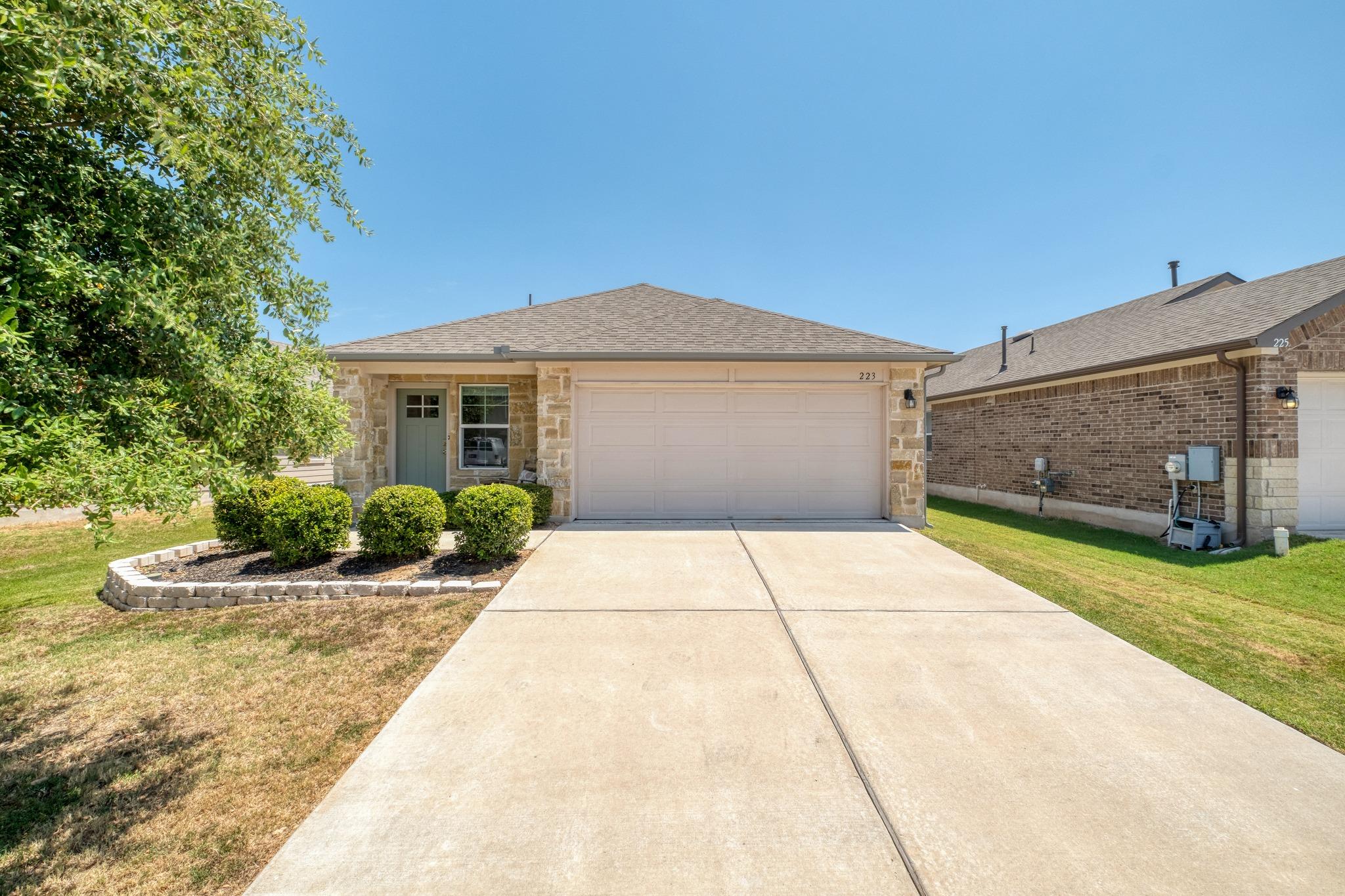 Single-story stone-and-siding home with a two-car garage, wide driveway, and trimmed front shrubs.