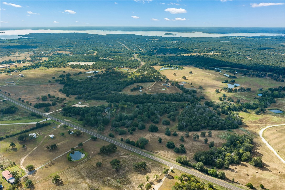 Aerial view of rural acreage with scattered ponds, a road, and a large lake on the horizon.