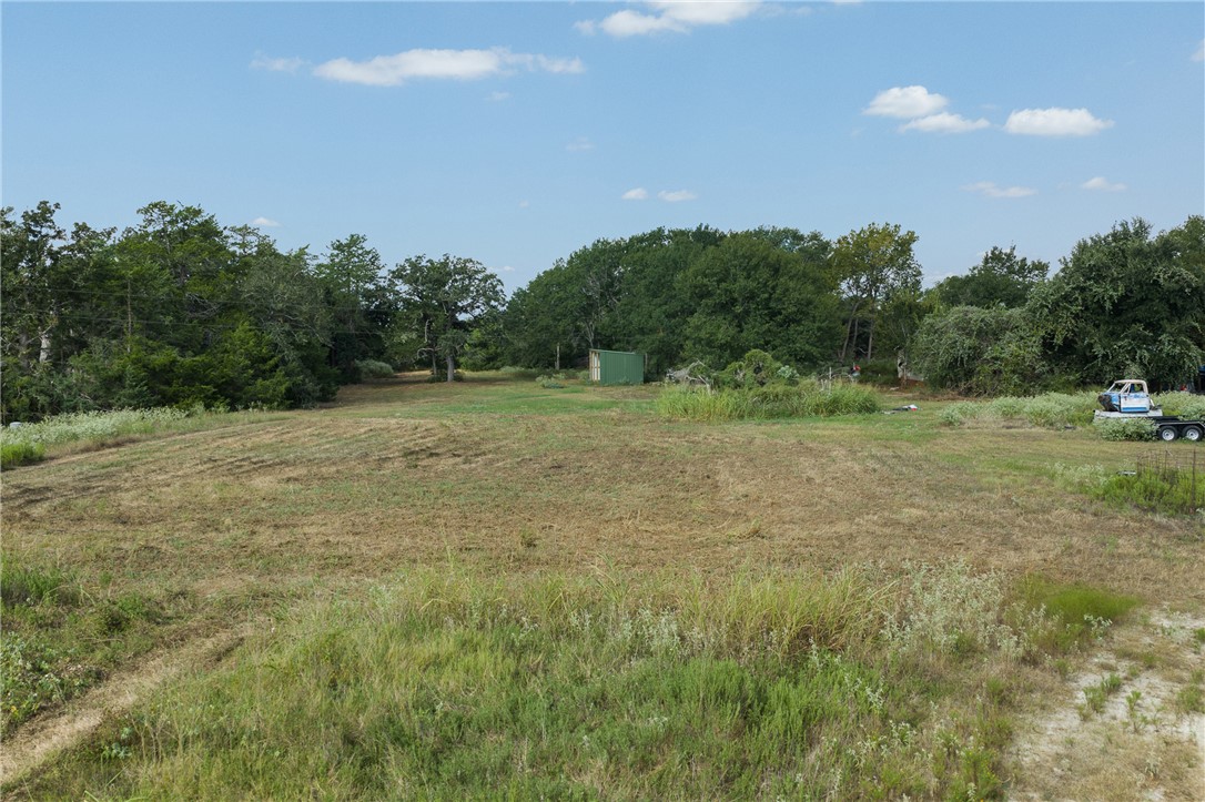 Cleared grassy property bordered by trees, with a green shed and equipment trailer near the back.