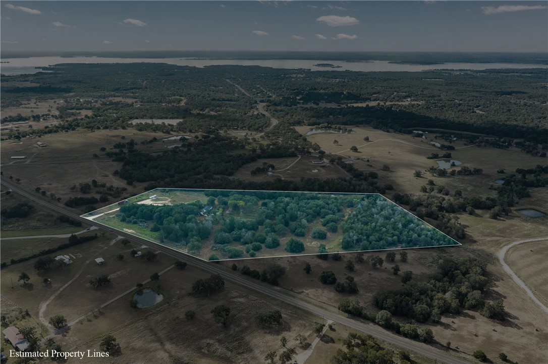 Aerial view of wooded acreage outlined beside a road, with water visible in the distance.
