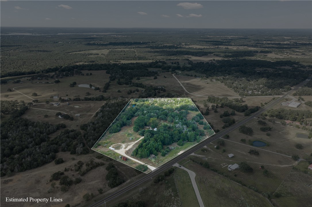 Aerial view of wooded acreage outlined beside a highway, with a driveway leading into the property.