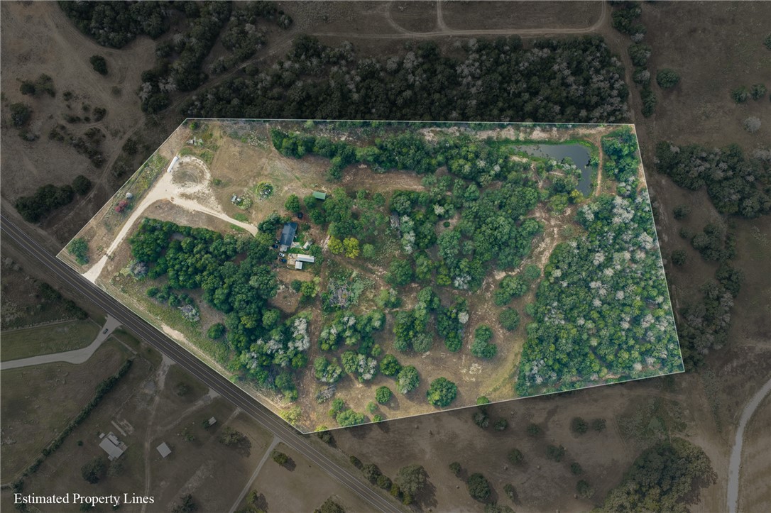 Aerial view of wooded acreage outlined by estimated property lines, with a pond, clearings, structures, and road frontage.