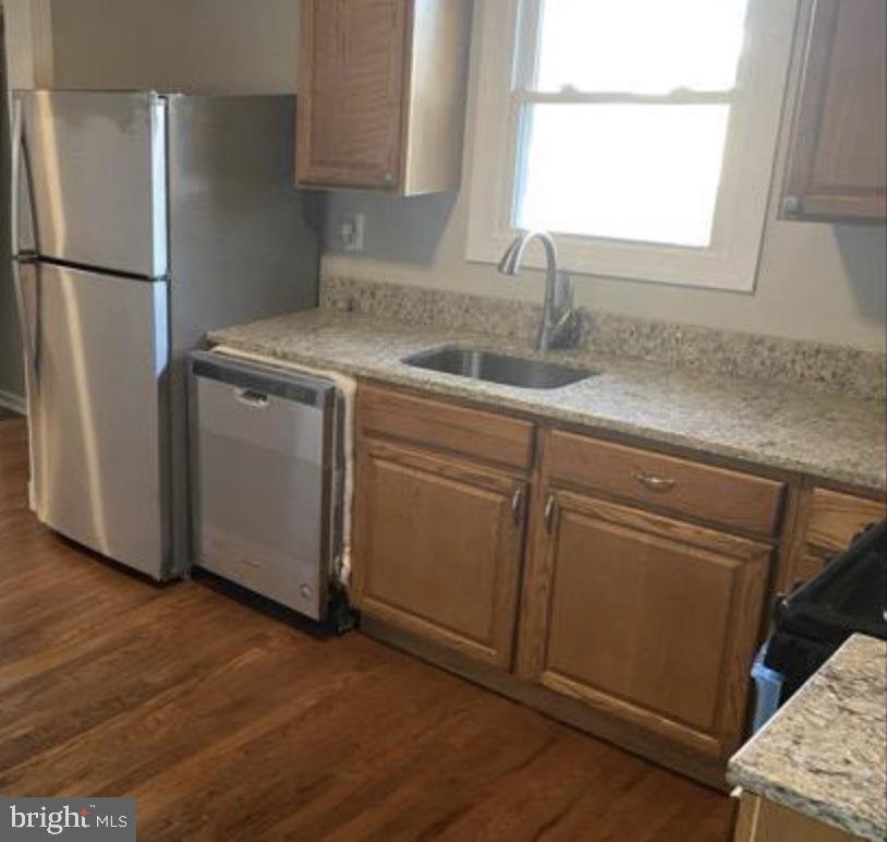 Kitchen with wood cabinets, speckled countertops, and a sink beneath a window.