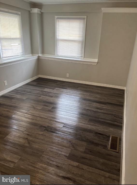 Empty room with two shaded windows and dark wood-look plank flooring.