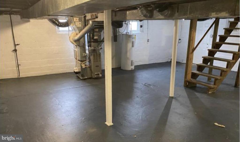 Unfinished basement with exposed ceiling joists, mechanical equipment, and open wooden stairs.