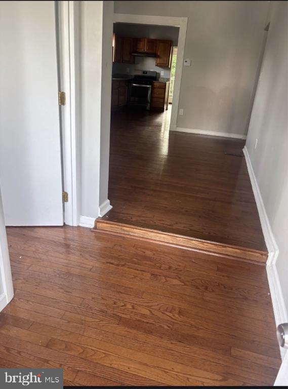 Empty hallway with hardwood floors leading to a kitchen with dark wood cabinets.