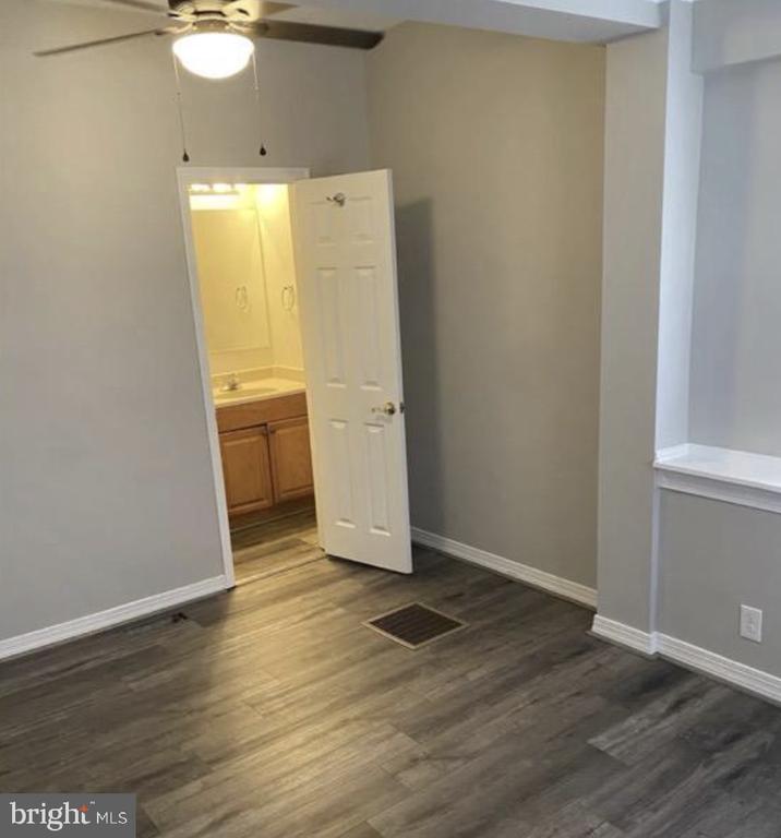 Empty room with gray wood-look flooring, ceiling fan, and open doorway to a bathroom.