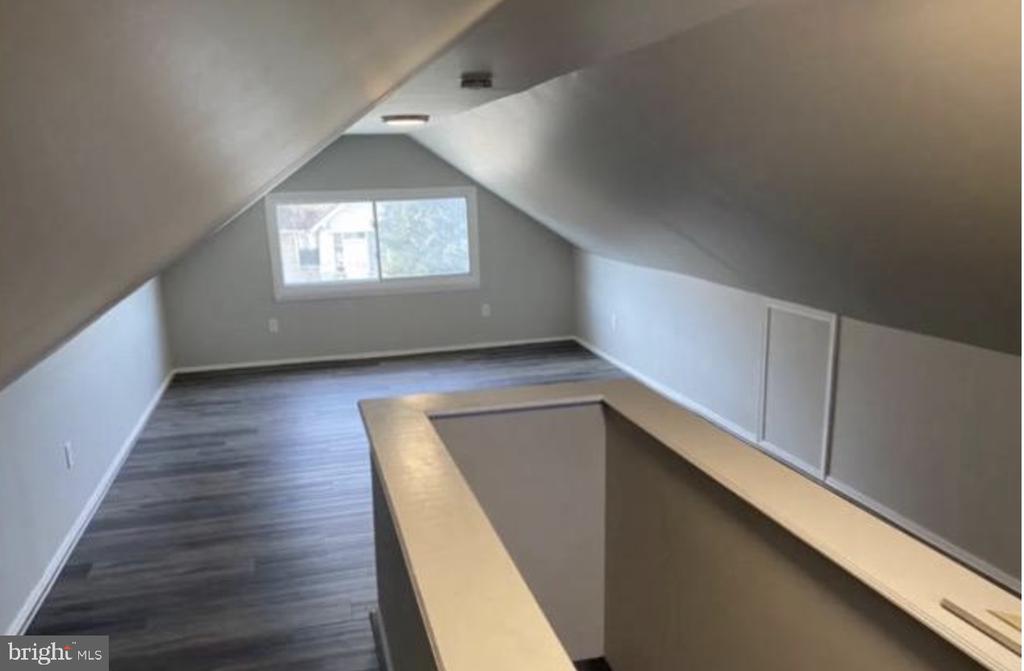 Unfurnished attic loft with sloped ceilings, gray plank flooring, and a wooden railing around the stairwell opening.