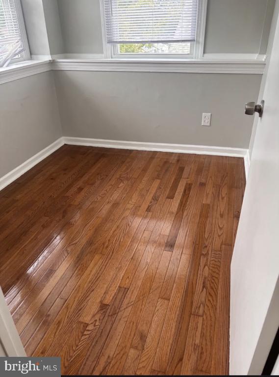 Vacant room with polished hardwood floors, gray walls, and windows with blinds.