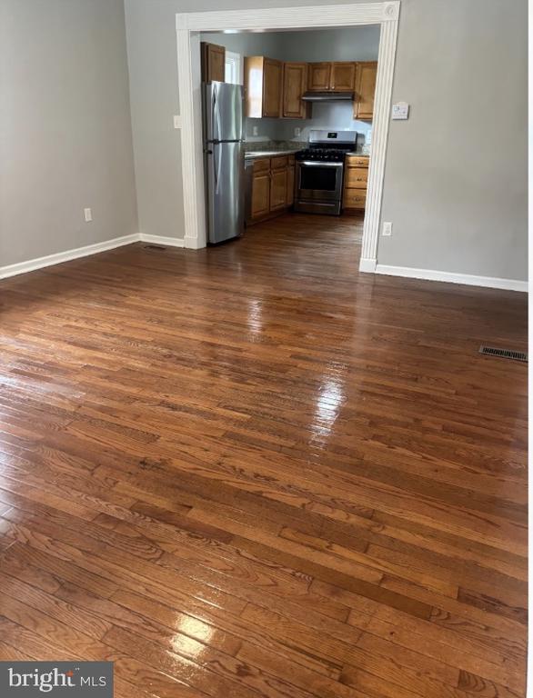 Living area with glossy hardwood floors and a doorway opening to a wood-cabinet kitchen.