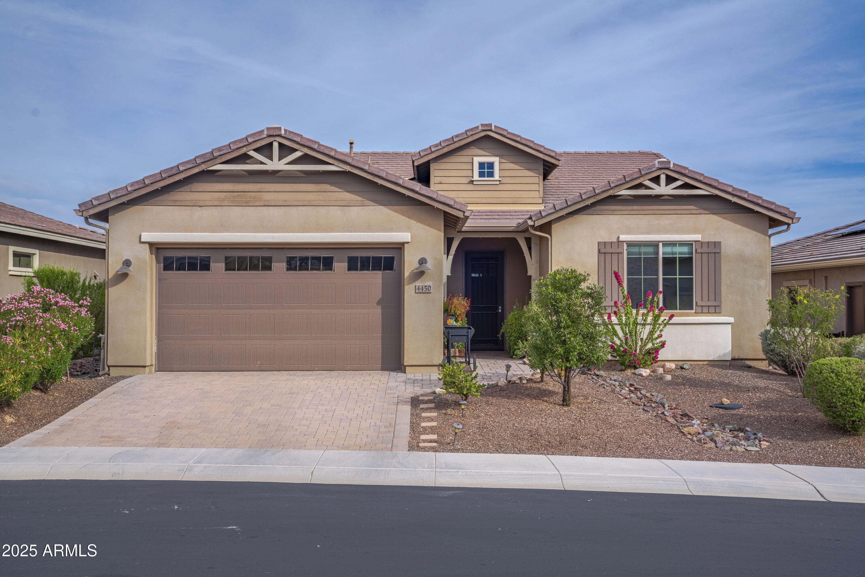 Tan stucco home with a tiled roof, two-car garage, covered entry, and flowering desert landscaping.