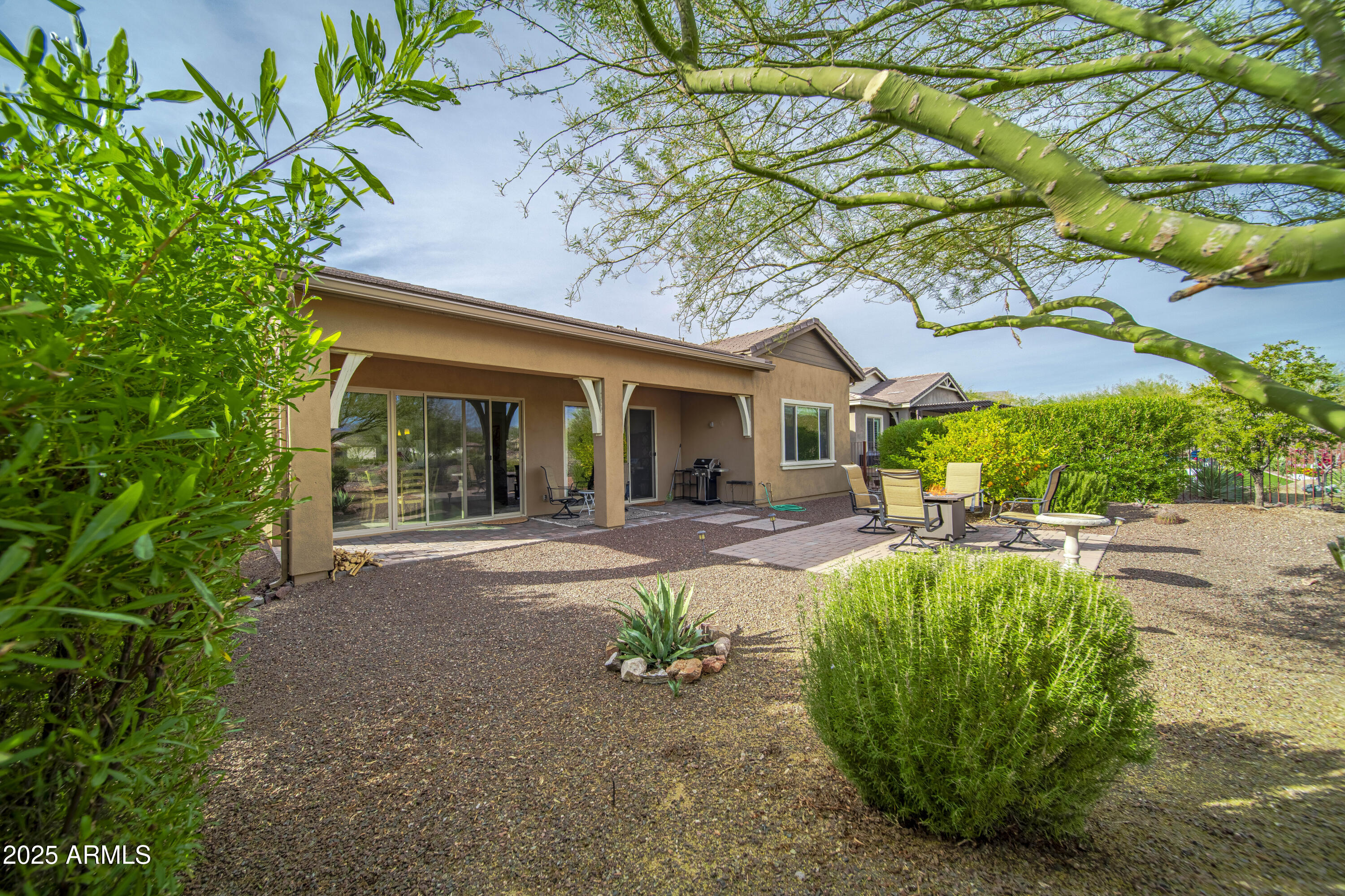Home’s covered rear patio and gravel yard with outdoor seating and desert landscaping.