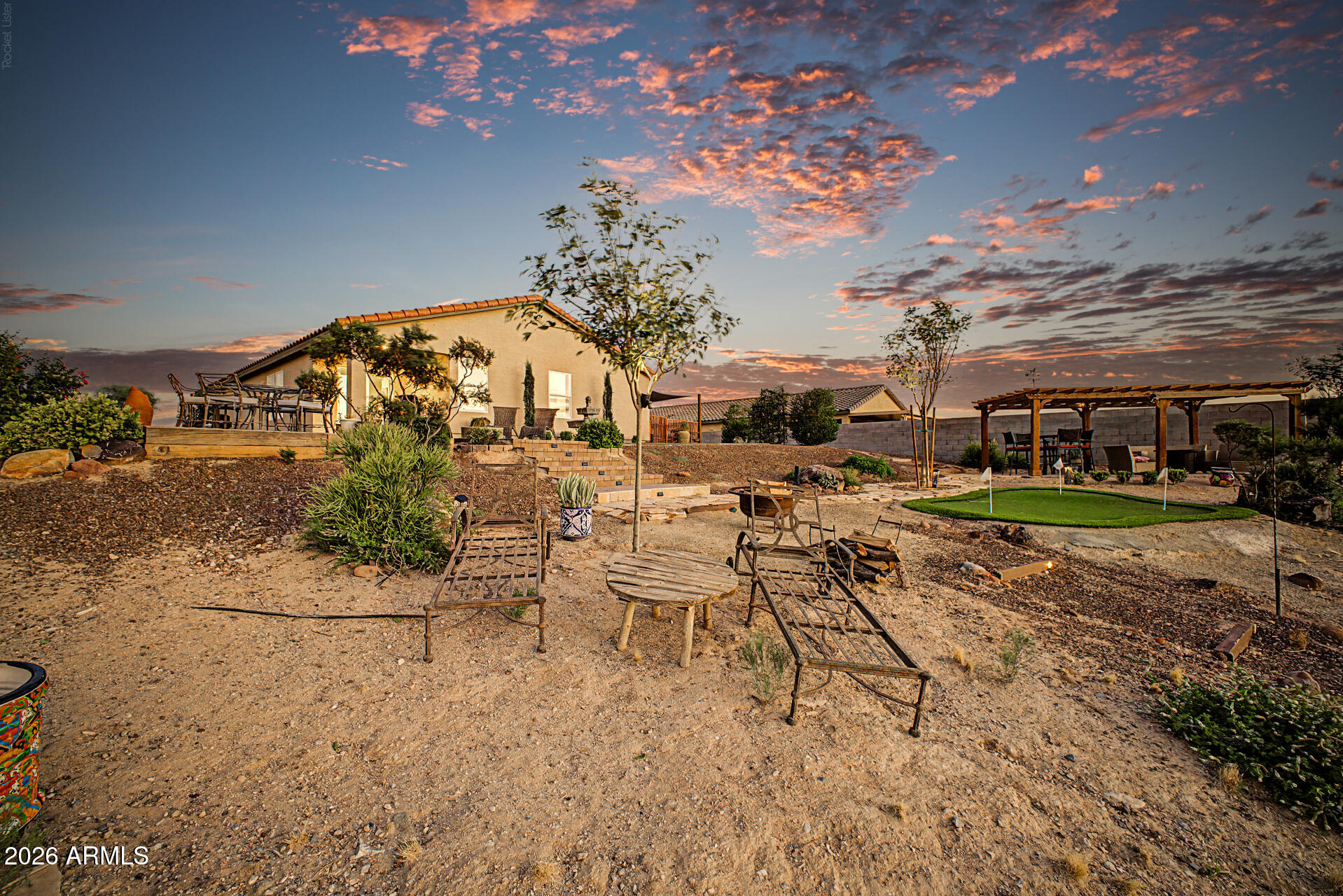 Desert backyard at sunset with outdoor seating, a pergola, and a small putting green.