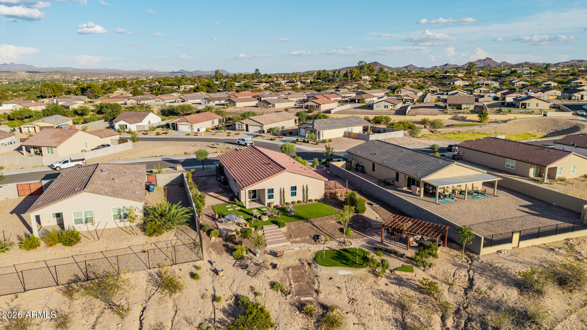 Aerial view of a Wickenburg home with a green backyard lawn, patio, putting green, and distant mountains.