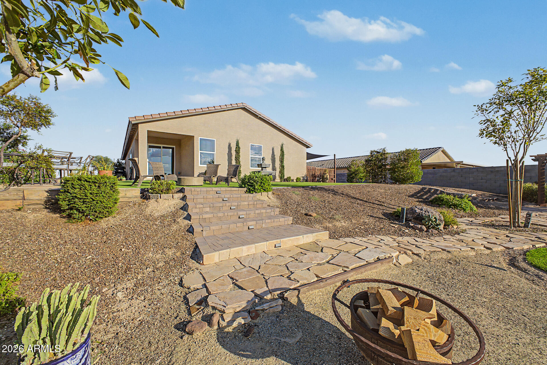 Home’s desert-landscaped backyard with raised patio, tiered paver steps, and flagstone path.